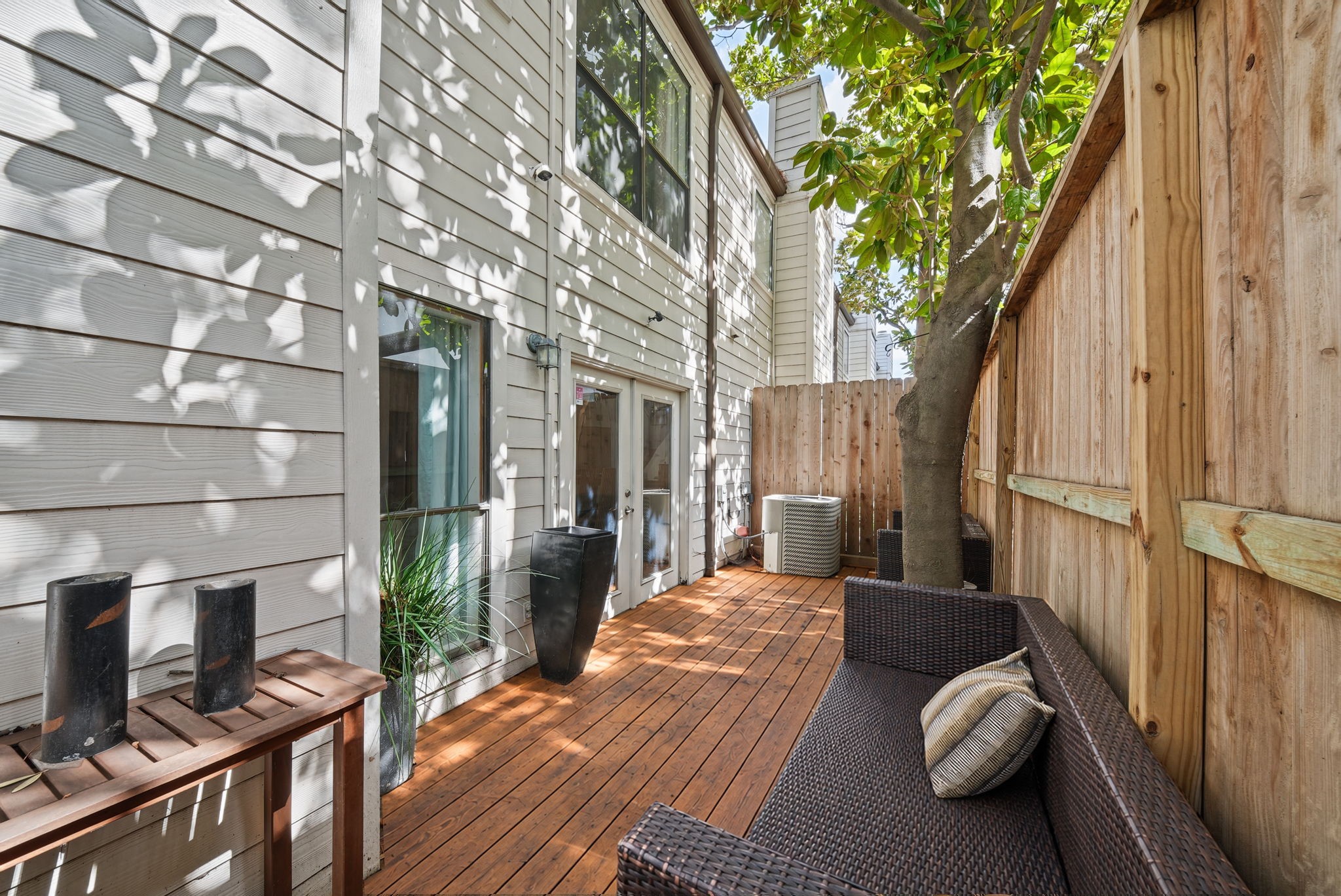 Charming private patio with wooden decking, shaded by a tree, offering a cozy outdoor seating area, perfect for evening relaxing or having your morning coffee outside.