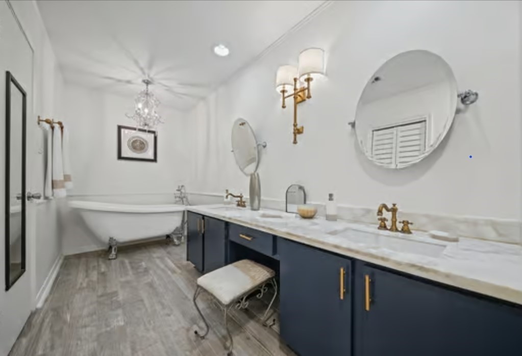 Elegant owner's suite bathroom featuring a classic clawfoot tub, dual sinks with marble countertops, and sophisticated gold fixtures, all illuminated by a stylish chandelier.