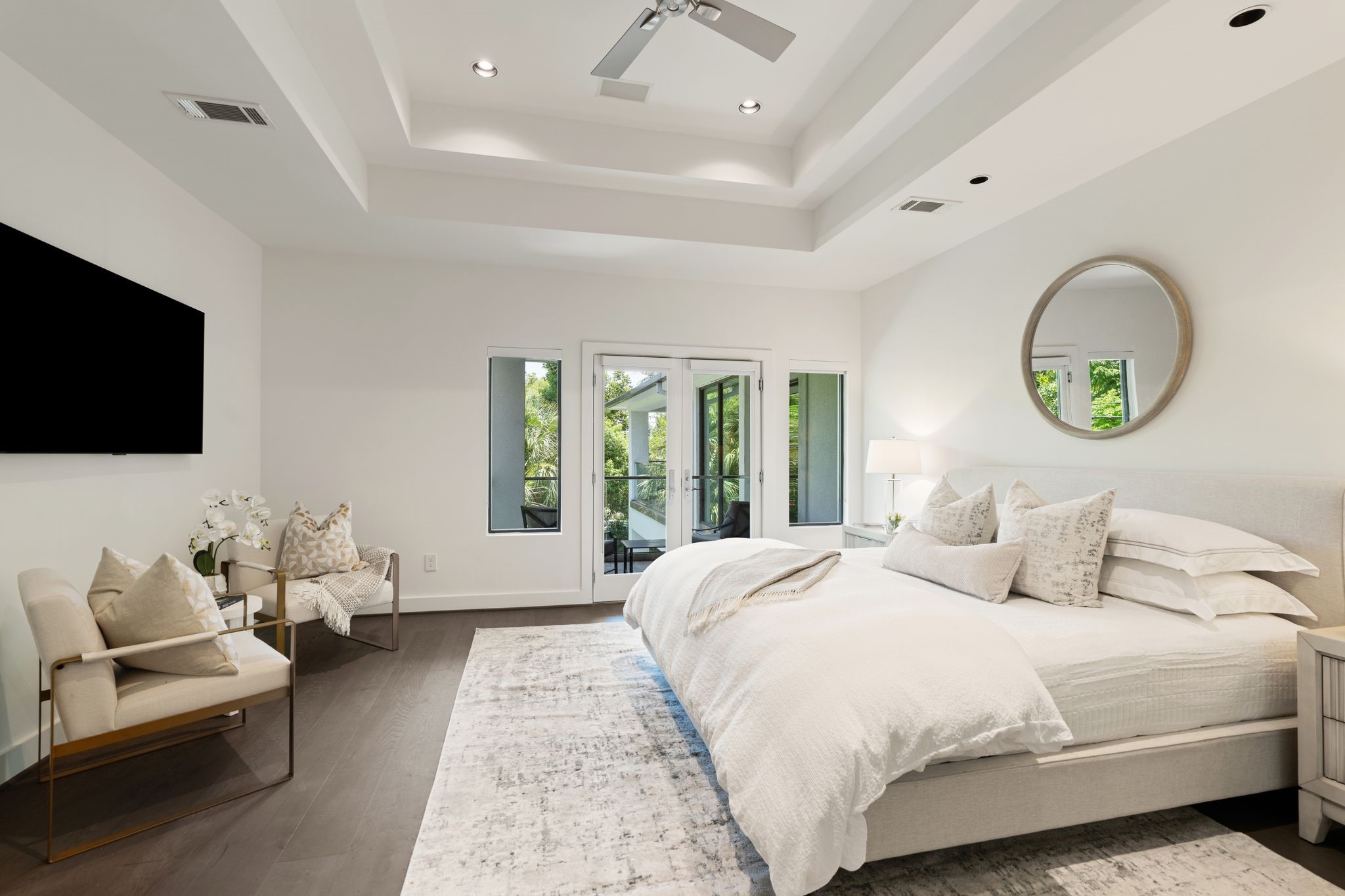 The spacious primary suite is a private retreat featuring a tray ceiling, serene sitting area, and a private balcony overlooking the resort-style pool and lush backyard.