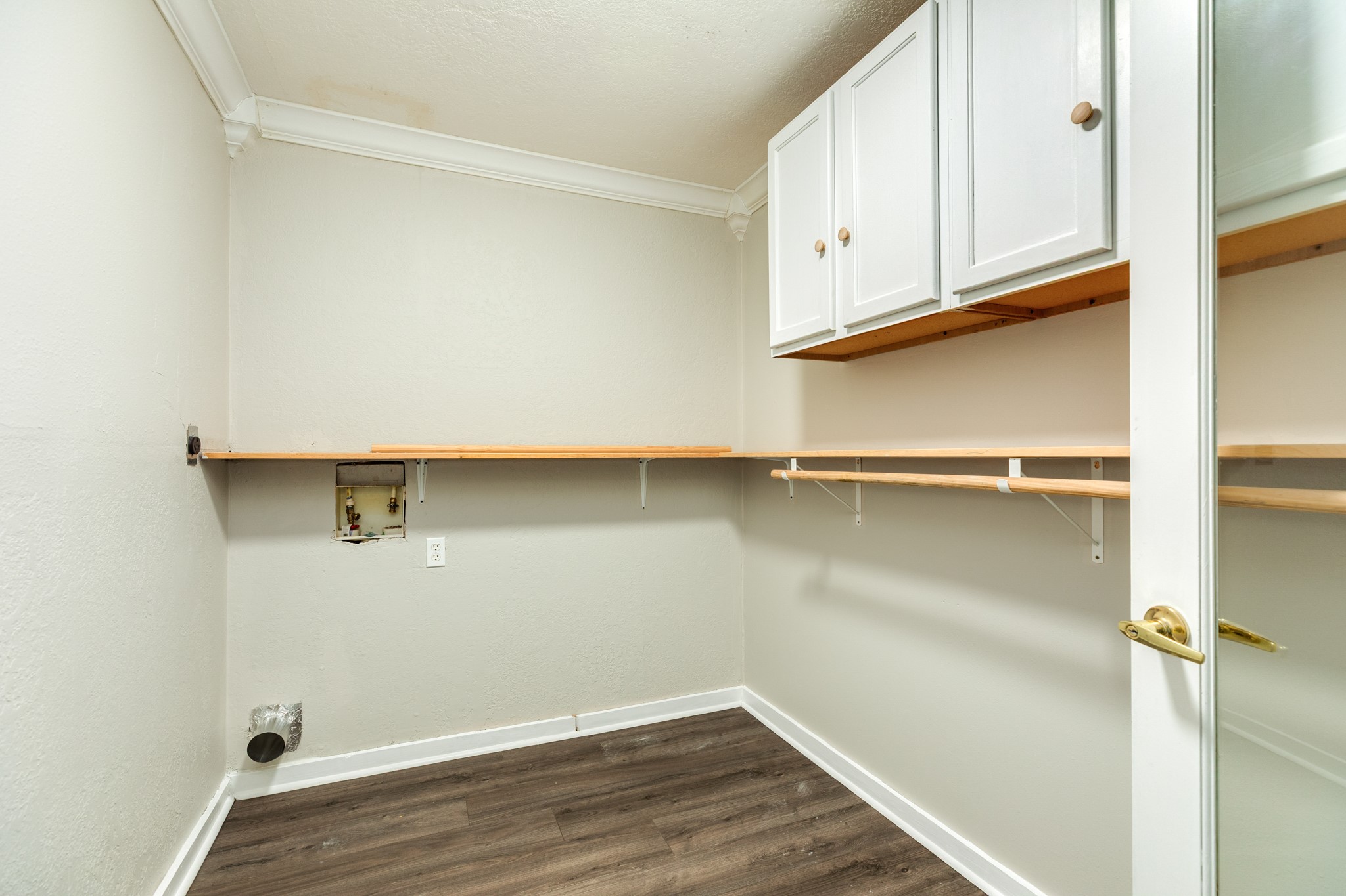 Dedicated laundry and utility space offers washer and dryer hookups, extensive open shelving, and overhead cabinetry for additional storage. Wood-look flooring and neutral finishes create a practical, versatile area.