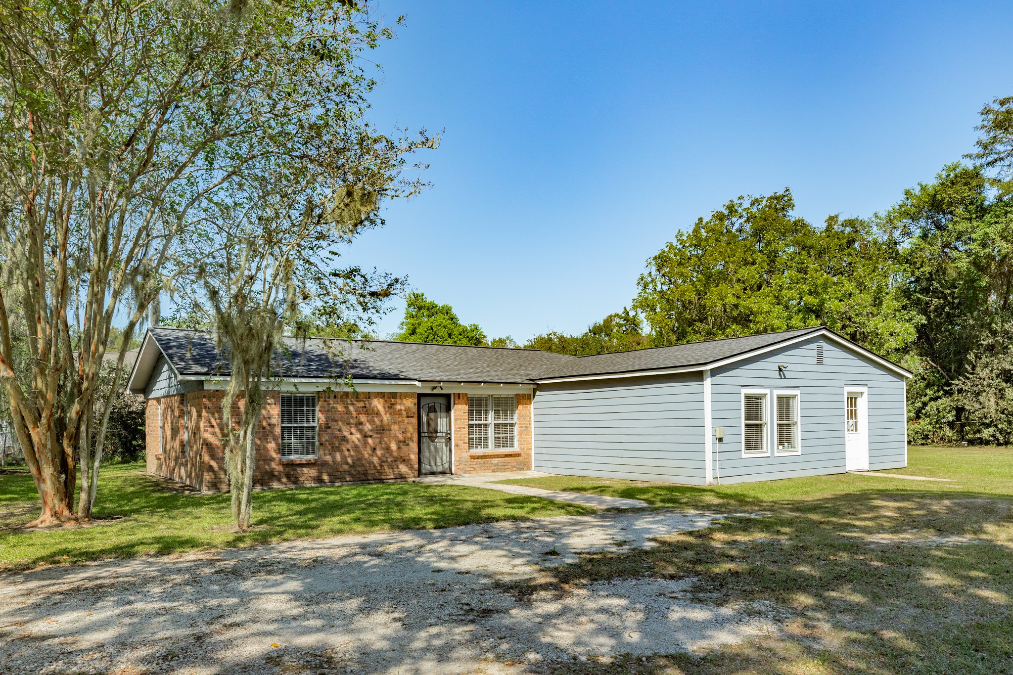 Attractive exterior showcases classic brickwork complemented by blue-gray horizontal siding, white trim, and a dark shingle roof. Mature trees and an open lawn create a peaceful, inviting setting.