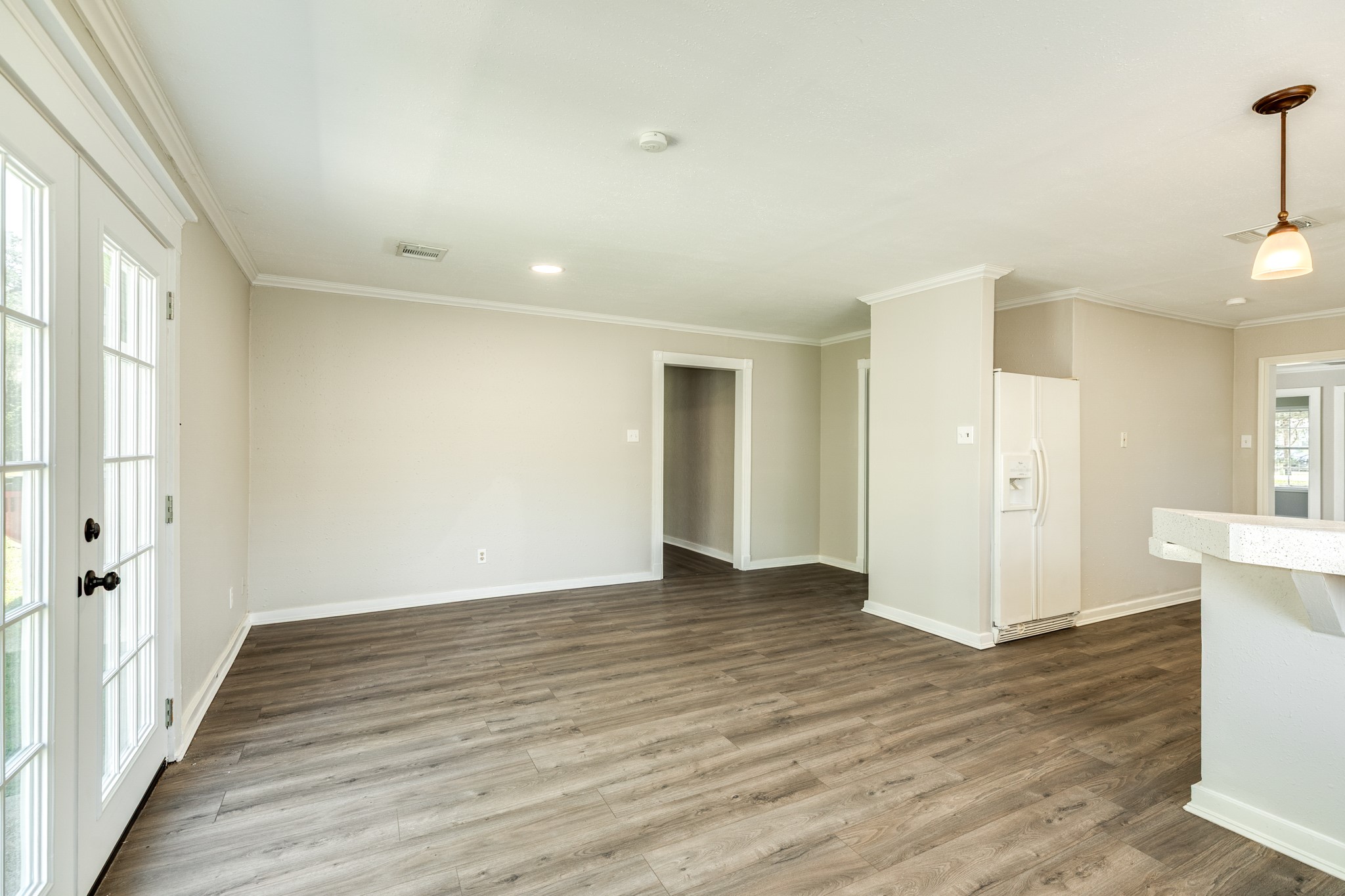 Open and versatile living and dining space showcases attractive wood-look flooring, neutral wall colors, and crown molding. French doors provide natural light and convenient access to the outdoors.