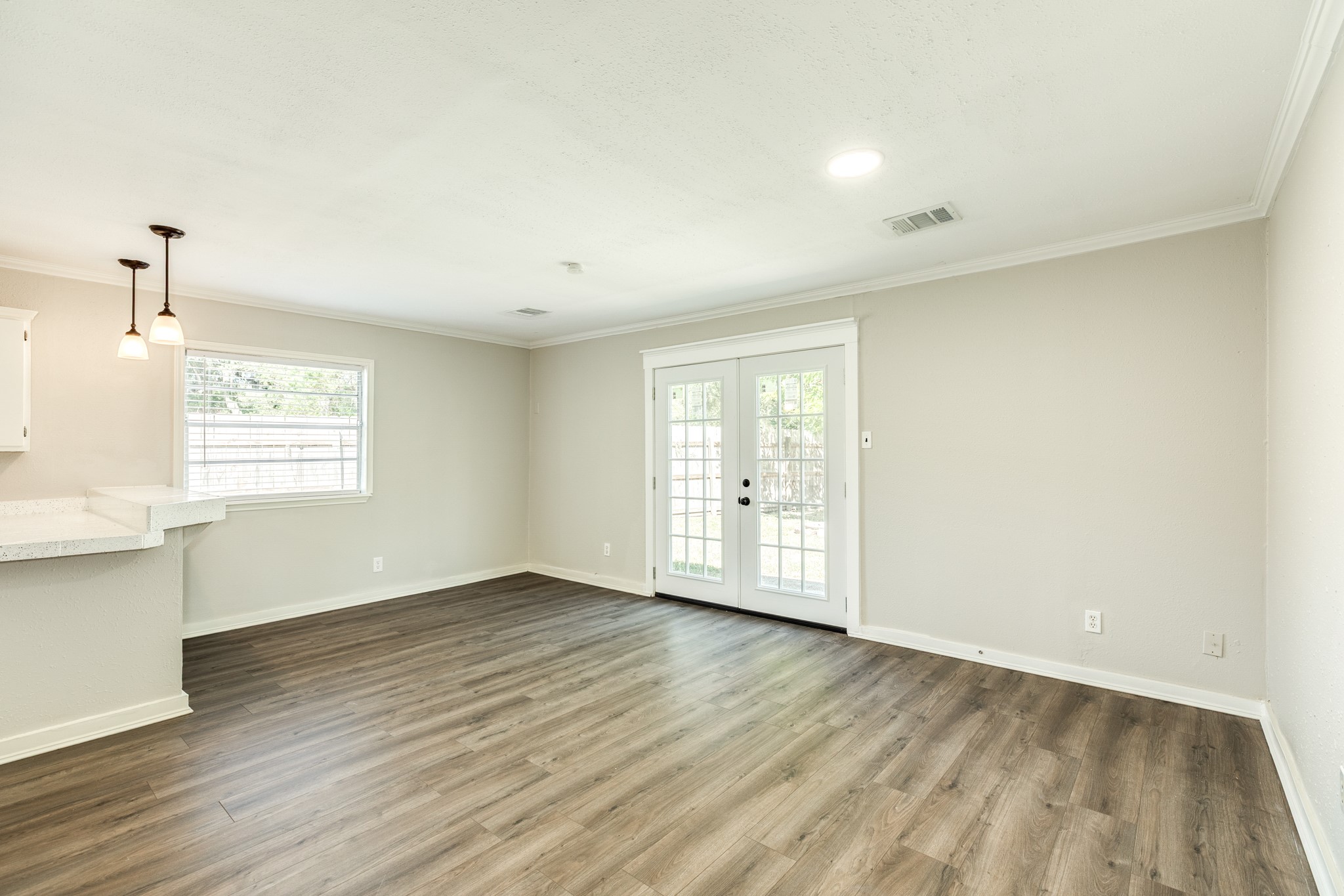 Spacious dining area offers flexible furniture arrangements, durable wood-look flooring, and French doors overlooking the outdoor space. A breakfast bar with pendant lighting provides a convenient connection to the kitchen.