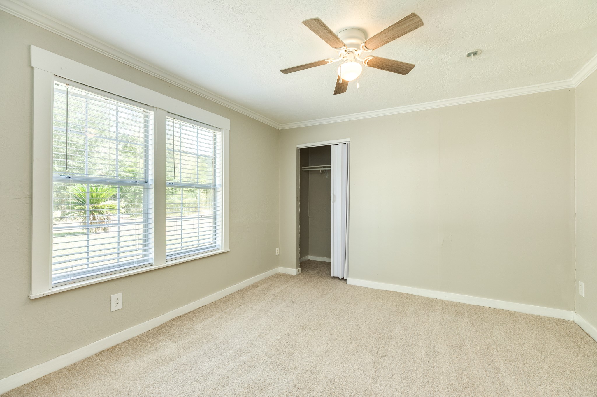 Inviting bedroom features soft neutral carpeting, two large windows with blinds, and a ceiling fan with lighting. A built-in closet with sliding doors provides convenient storage.