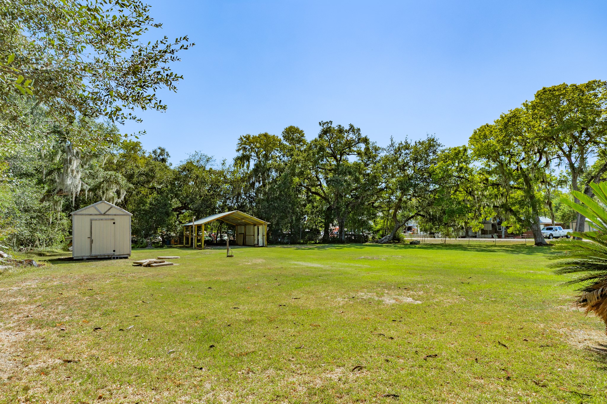 Generous open yard features mature trees, a freestanding storage shed, and a separate covered structure. The expansive grassy setting offers flexibility for outdoor recreation, gardening, and equipment storage.