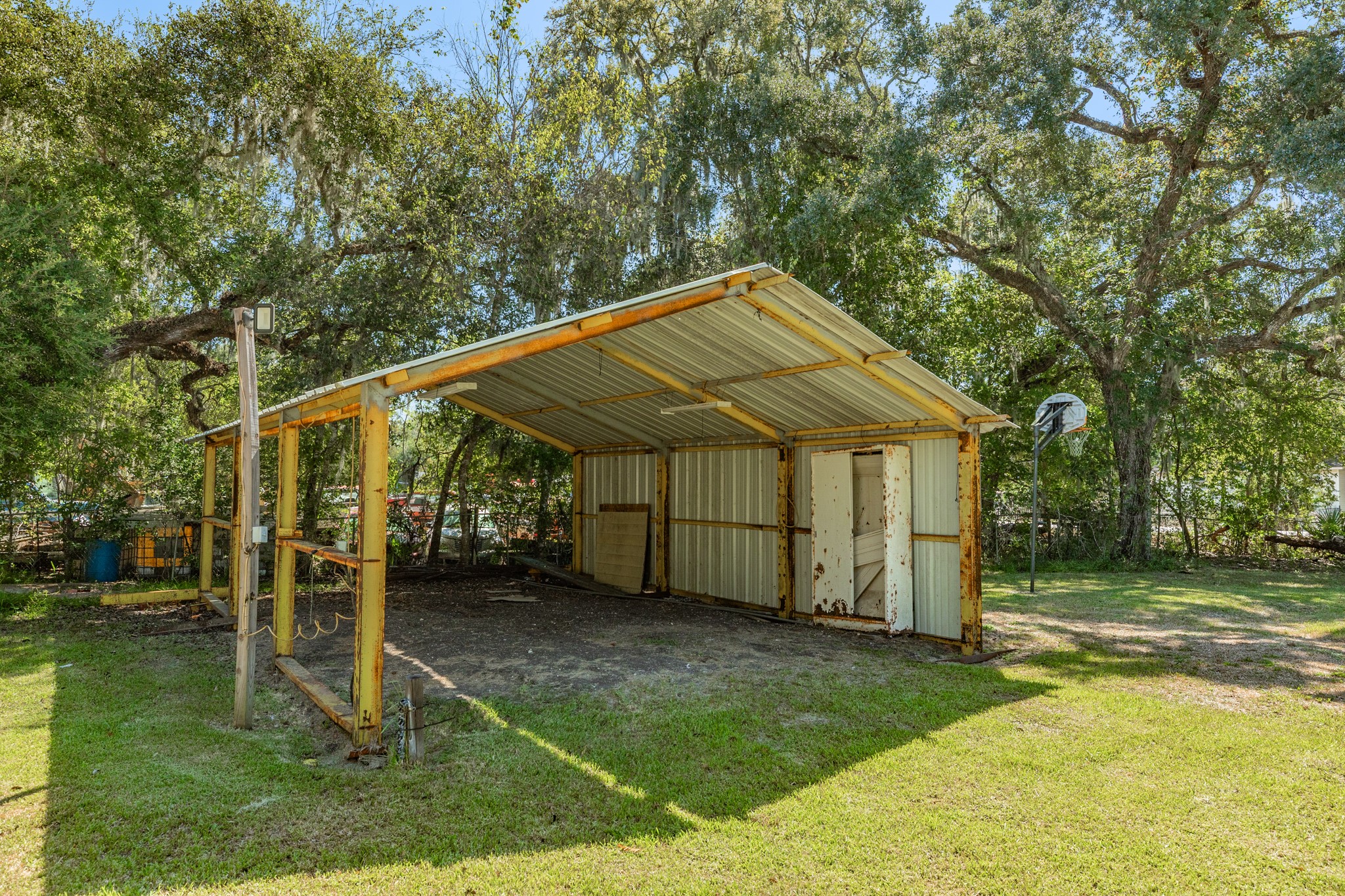 Freestanding metal-roofed structure offers a spacious covered area with open sides, a partially enclosed rear section, and overhead lighting. Ideal for a variety of outdoor storage or workspace needs.