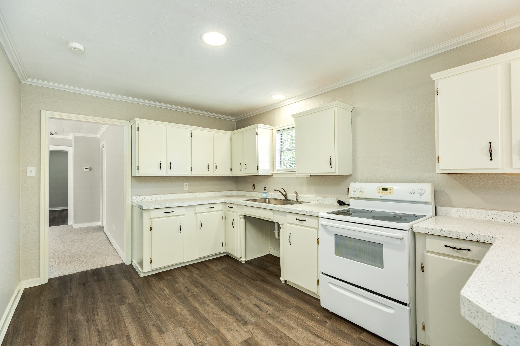 Functional kitchen layout offers abundant white cabinetry, generous counter space, and a white electric range. Recessed lighting, crown molding, and wood-look flooring complete the bright, neutral design.