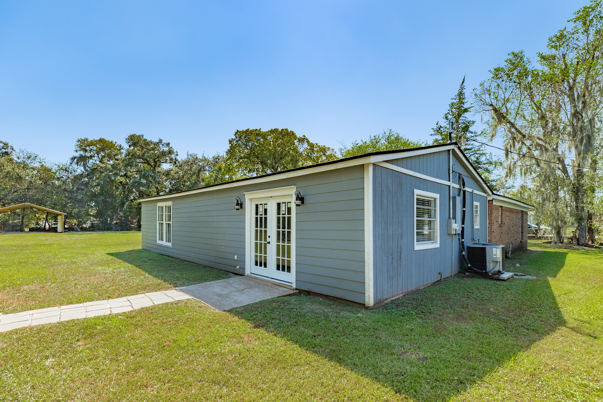 Rear view showcases blue-gray siding, white-trimmed French doors, exterior lighting, and a concrete landing. The adjoining lawn offers easy access to the home's outdoor gathering areas.