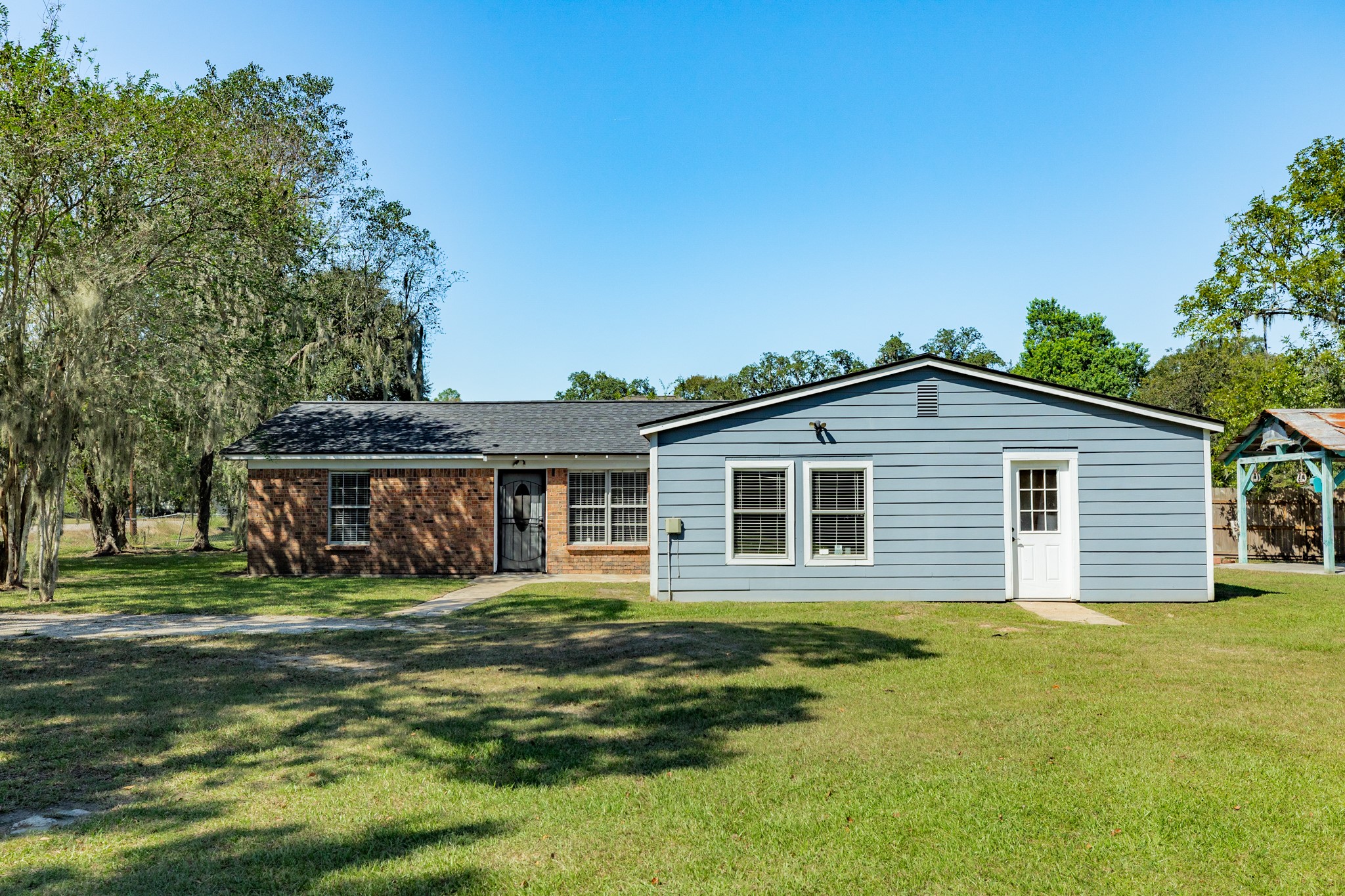 Spacious single-story home offers a distinctive combination of brick and blue-gray siding, with multiple windows welcoming natural light. An expansive grassy lawn provides plenty of room for outdoor activities.