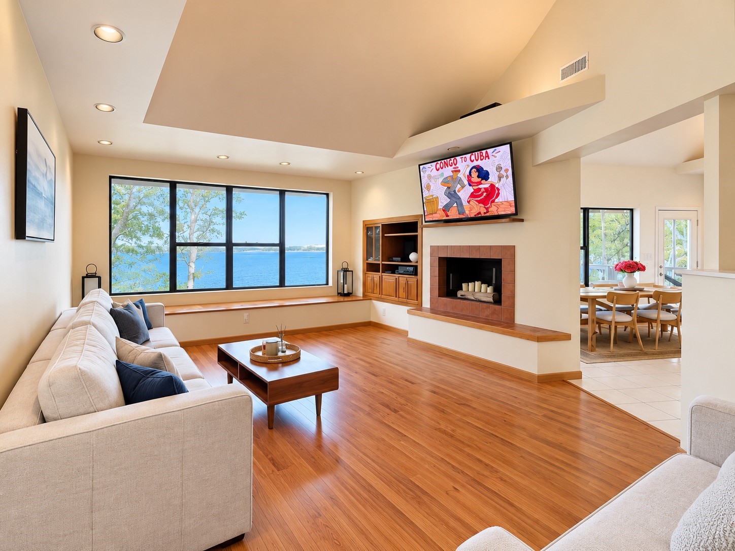 Spacious living room with stunning lake views, featuring a cozy fireplace, elegant hardwood floors, and an open layout connecting to the dining area.