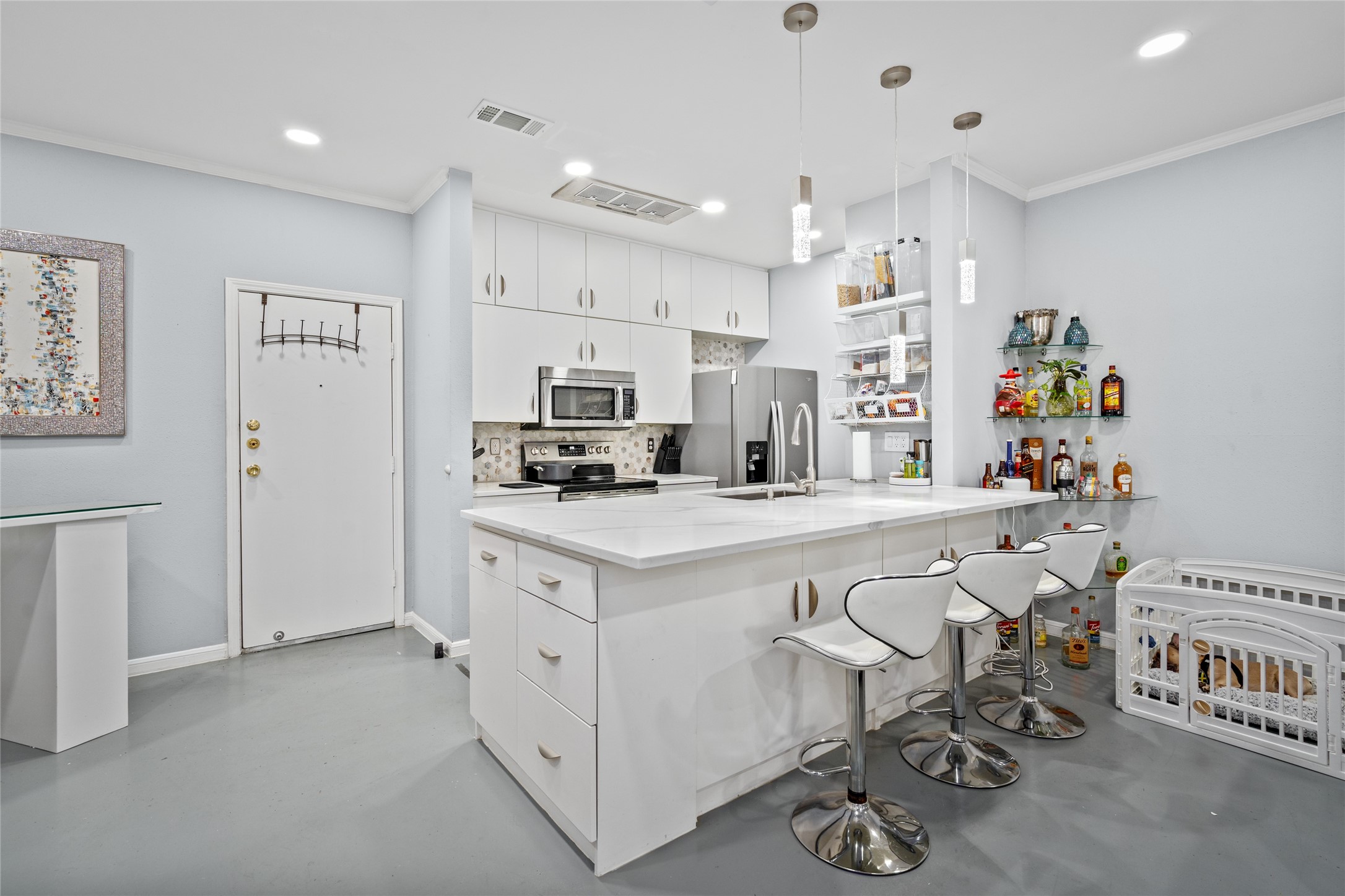This stylish and functional kitchen features sleek white cabinetry, stainless steel appliances, and a stunning quartz countertop island with a breakfast bar. Pendant lighting adds a contemporary touch, while open shelving provides convenient storage. The adjacent bar area offers additional space for entertaining, making this kitchen perfect for hosting and everyday living.