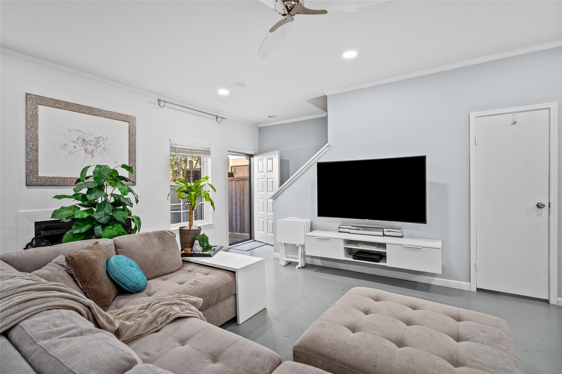 This inviting living room offers a spacious, open-concept design with modern finishes and a neutral color palette. Natural light streams in through the large window, creating a warm and welcoming atmosphere. The front door provides easy access, while the nearby staircase leads to the upper level. Recessed lighting and a sleek ceiling fan enhance the contemporary feel. A conveniently located half-bathroom is tucked away for guests, adding to the functionality of the space.