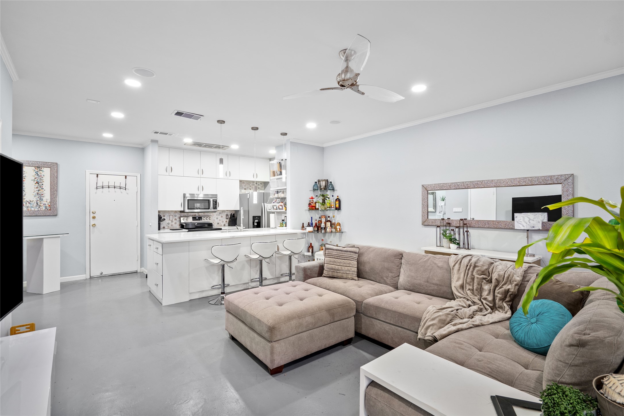 This beautifully designed open-concept space seamlessly blends the kitchen and living area, creating an inviting atmosphere for both cooking and entertaining. The sleek white island with a waterfall quartz countertop serves as a focal point, complemented by elegant pendant lighting. The spacious living area features a plush sectional sofa, large windows for natural light, and modern finishes, making it the perfect space to relax and unwind.