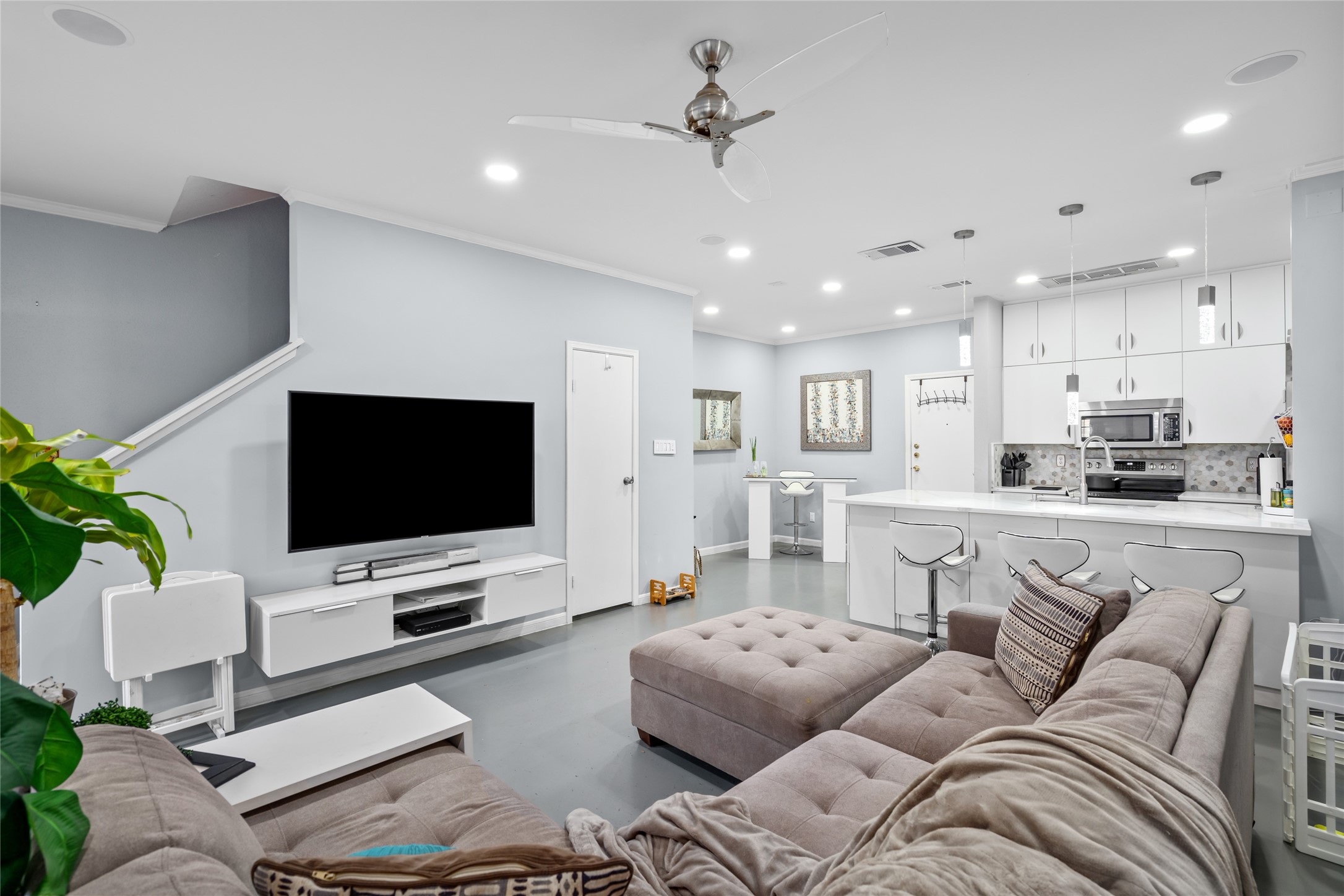 This beautifully designed open-concept living space seamlessly connects to the modern kitchen, creating an ideal layout for both relaxation and entertaining. The spacious living area features recessed lighting, a sleek ceiling fan, and a neutral color palette that enhances the home's contemporary feel. The kitchen boasts crisp white cabinetry, stylish pendant lighting, and a large island with bar seatingperfect for casual dining or gathering with guests.