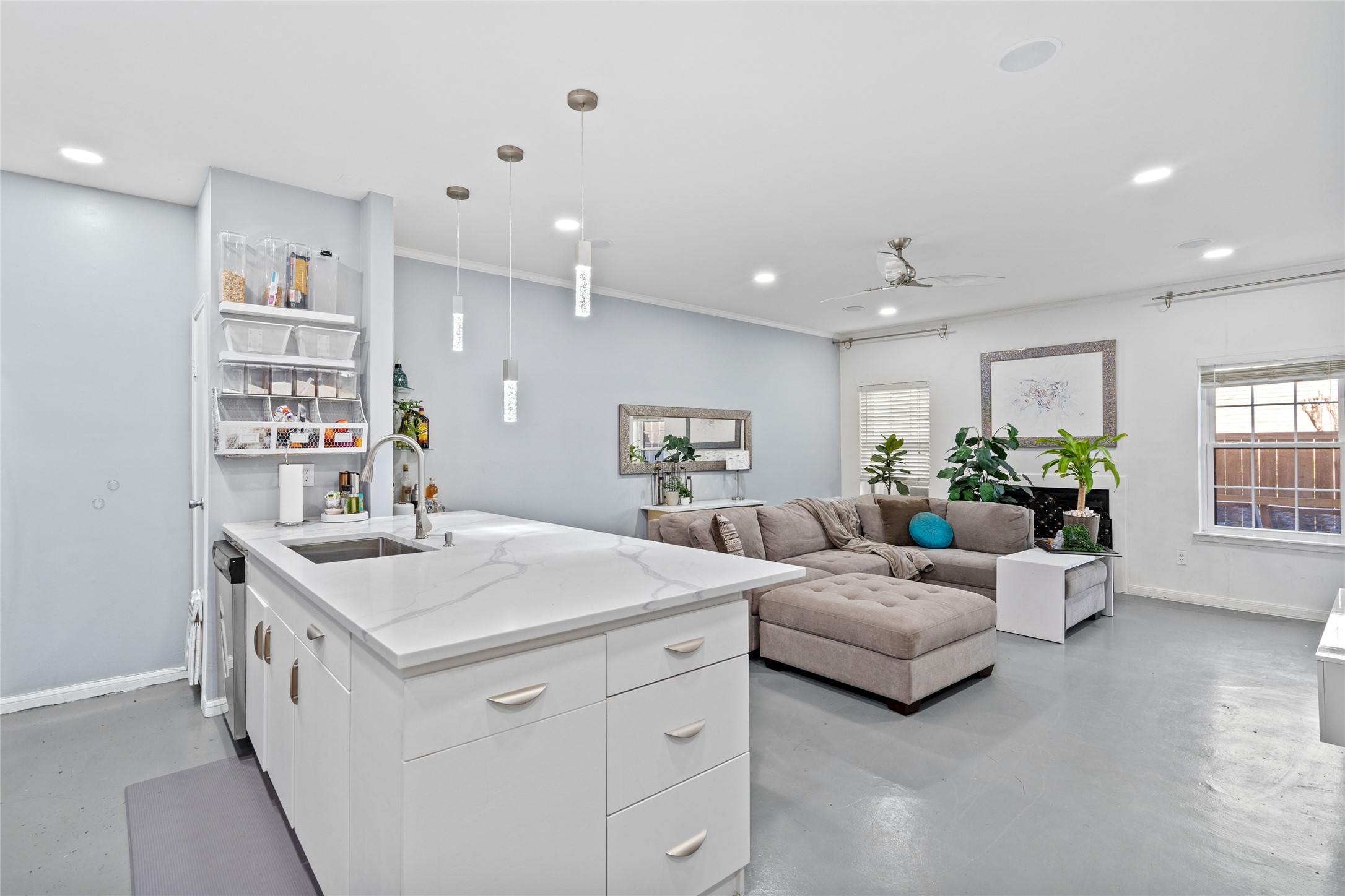 This beautifully designed open-concept space seamlessly blends the kitchen and living area, creating an inviting atmosphere for both cooking and entertaining. The sleek white island with a waterfall quartz countertop serves as a focal point, complemented by elegant pendant lighting. The spacious living area features a plush sectional sofa, large windows for natural light, and modern finishes, making it the perfect space to relax and unwind.