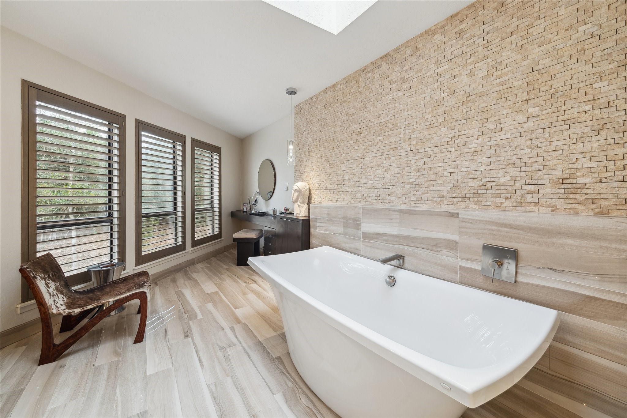 A soaking tub set against a dramatic stone accent wall, bathed in natural light from the skylight, complemented by a sophisticated separate vanity area designed for ultimate relaxation.