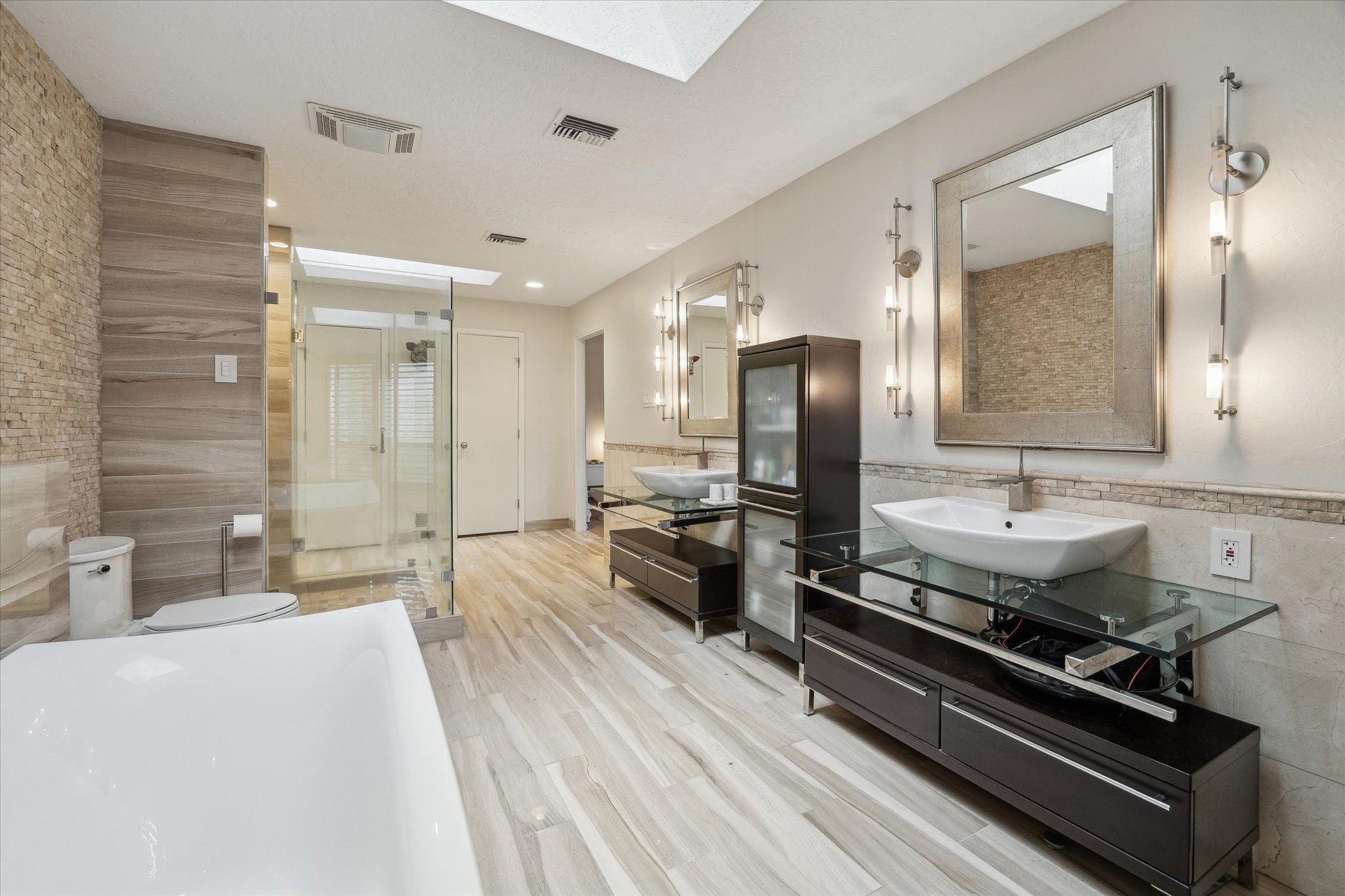 This ultra-luxe ensuite bath evokes a private spa experience, featuring dual vanities, soaking tub and a seamless glass shower; enhanced by natural light and a tranquil, elevated ambiance.
