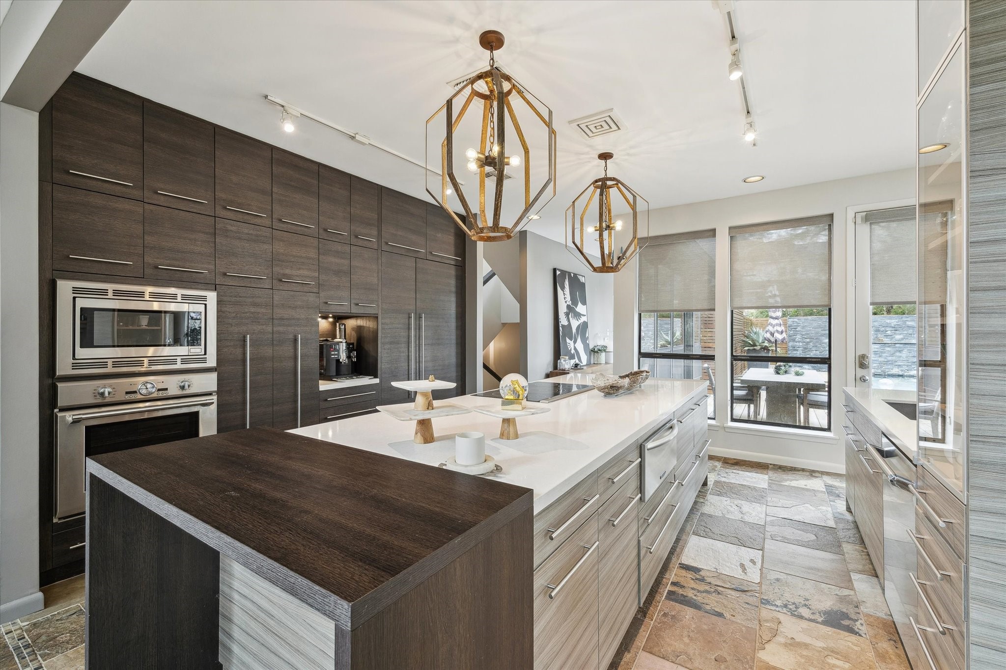 The kitchen flows seamlessly to the adjacent dining area and outdoor space through oversized windows, filling the room with natural light and creating an effortless indoor-outdoor connection.
