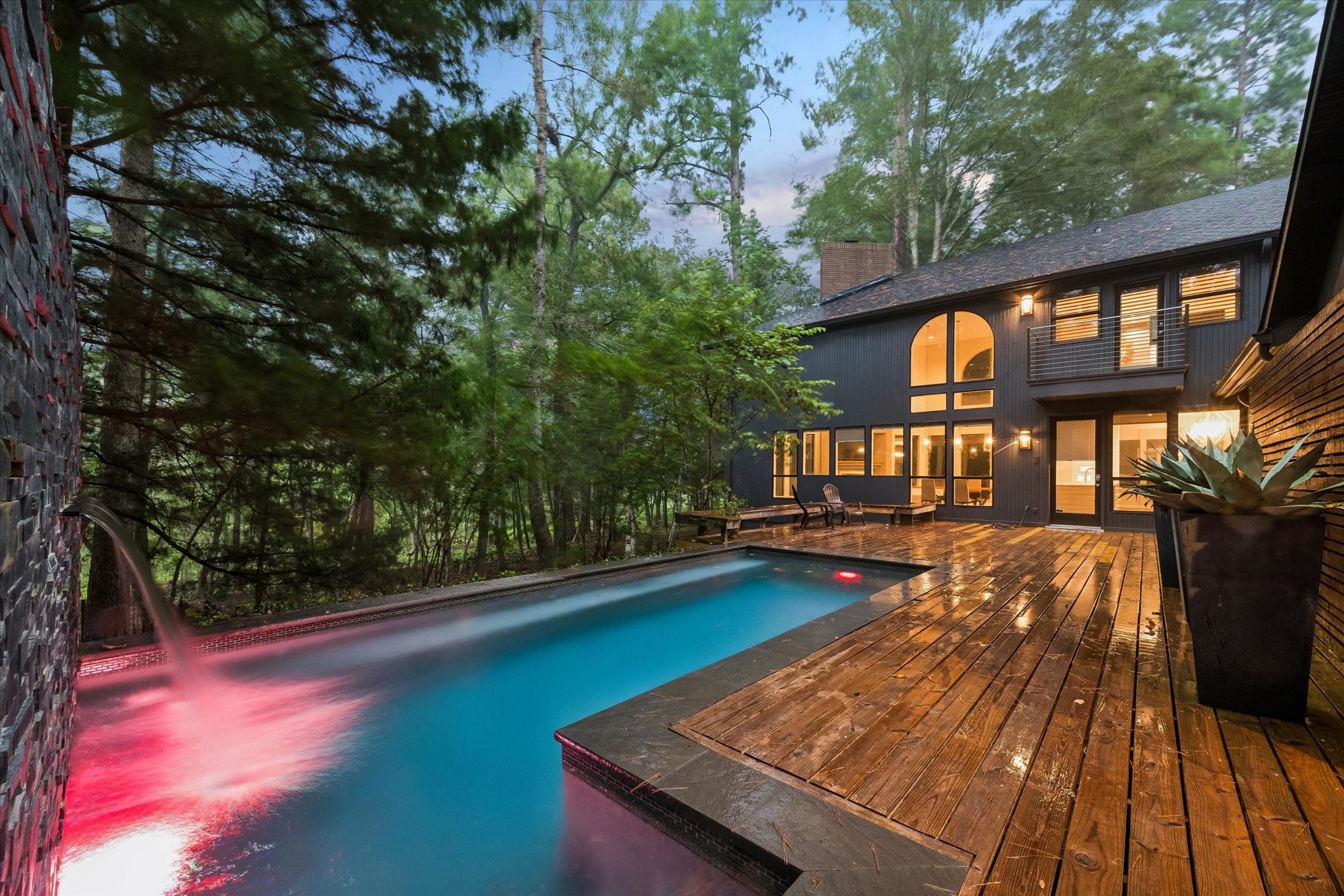 A raised water feature cascades into the pool below, adding both sound and sparkle to this wooded backyard retreat. The expansive wood deck wraps the pool's edge, offering plenty of room to lounge while taking in the home's striking vertical-plank architecture. A raised water feature cascades into the pool below, adding both sound and sparkle to this wooded backyard retreat. The expansive wood deck wraps the pool's edge, offering plenty of room to lounge while taking in the home's striking vertical-plank architecture.
