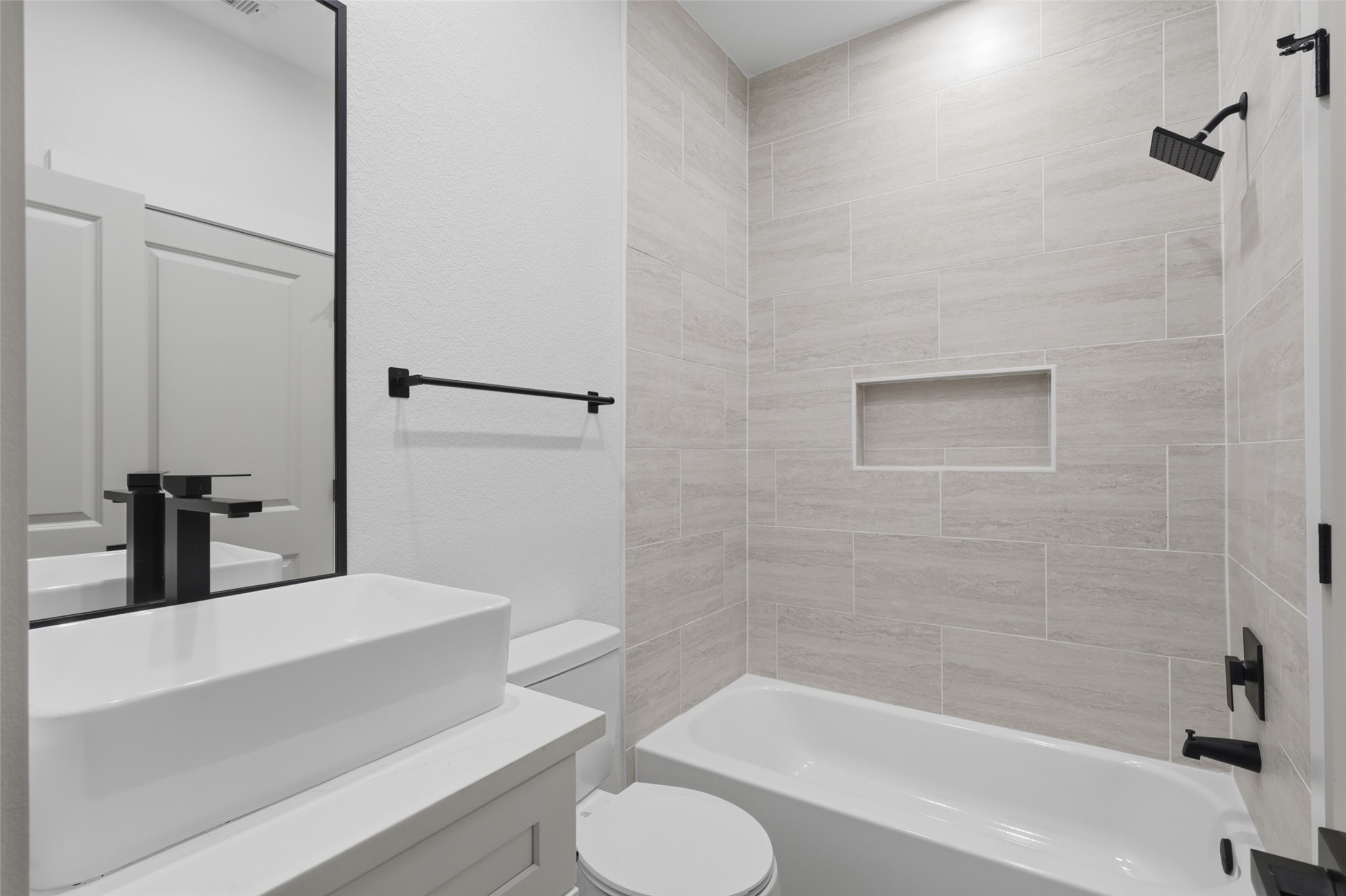 One of the many modern bathroom featuring sleek black fixtures, a spacious vanity with a vessel sink, and a tiled shower with an inset shelf for added convenience.