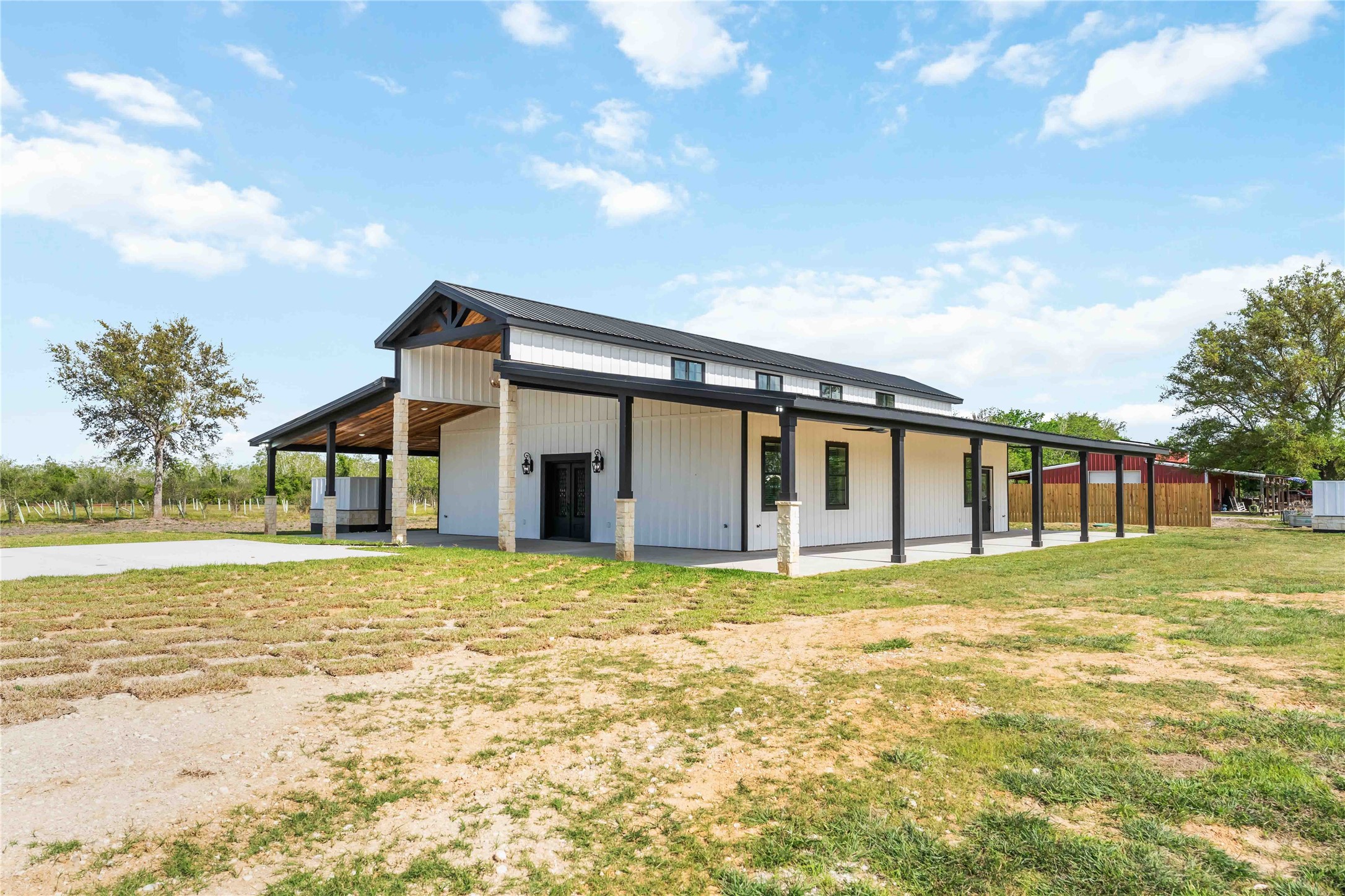 Modern farmhouse with a sleek black and white exterior, expansive covered porch, and surrounded by open land. Ideal for those seeking a blend of rustic charm and contemporary design.