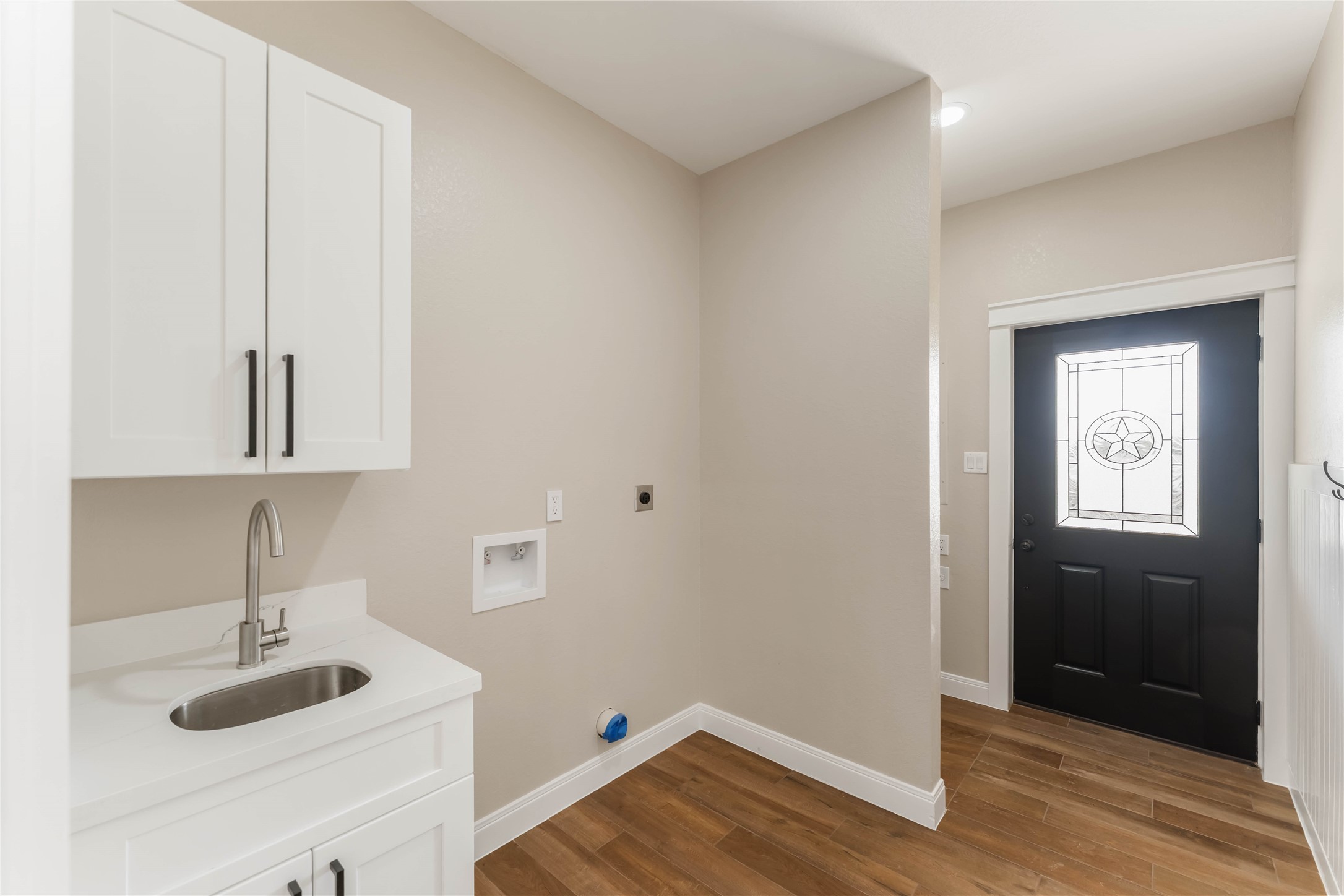 This room is the utility room that allows access to the outdoor wrap-around porch. It includes tile wood-style flooring with a drain, hand washing sink and storage cabinets. On the other side of the wall are hooks to hang coats or use for additional storage.