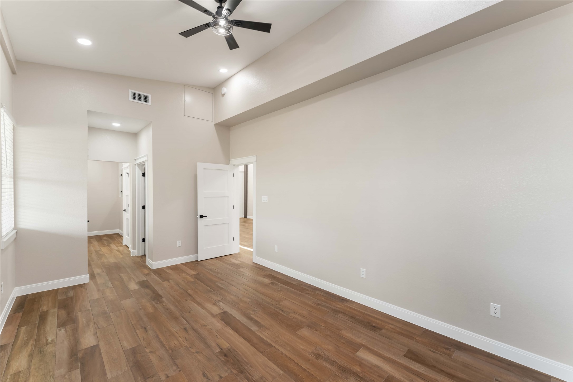 Bright and spacious room with high ceilings, tile wood-style flooring, and recessed lighting. Features a ceiling fan and multiple doors leading to other areas, offering a modern and open feel.