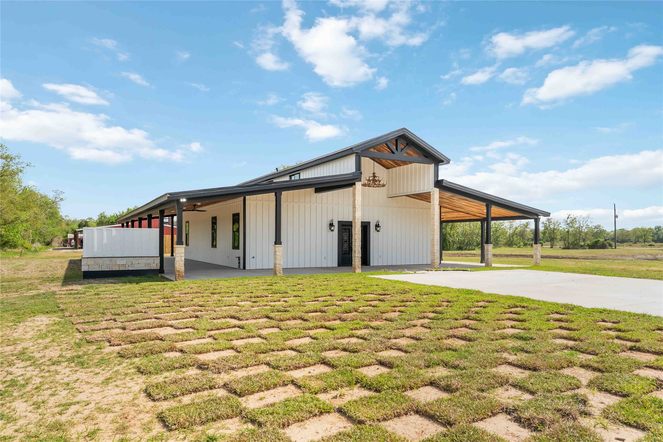 This modern farmhouse features a spacious, open design with a blend of rustic and contemporary elements. It boasts a large covered porch, ample natural light, and a rustic wood and metal exterior, set against a backdrop of open land. Perfect for those seeking a blend of style and tranquility.