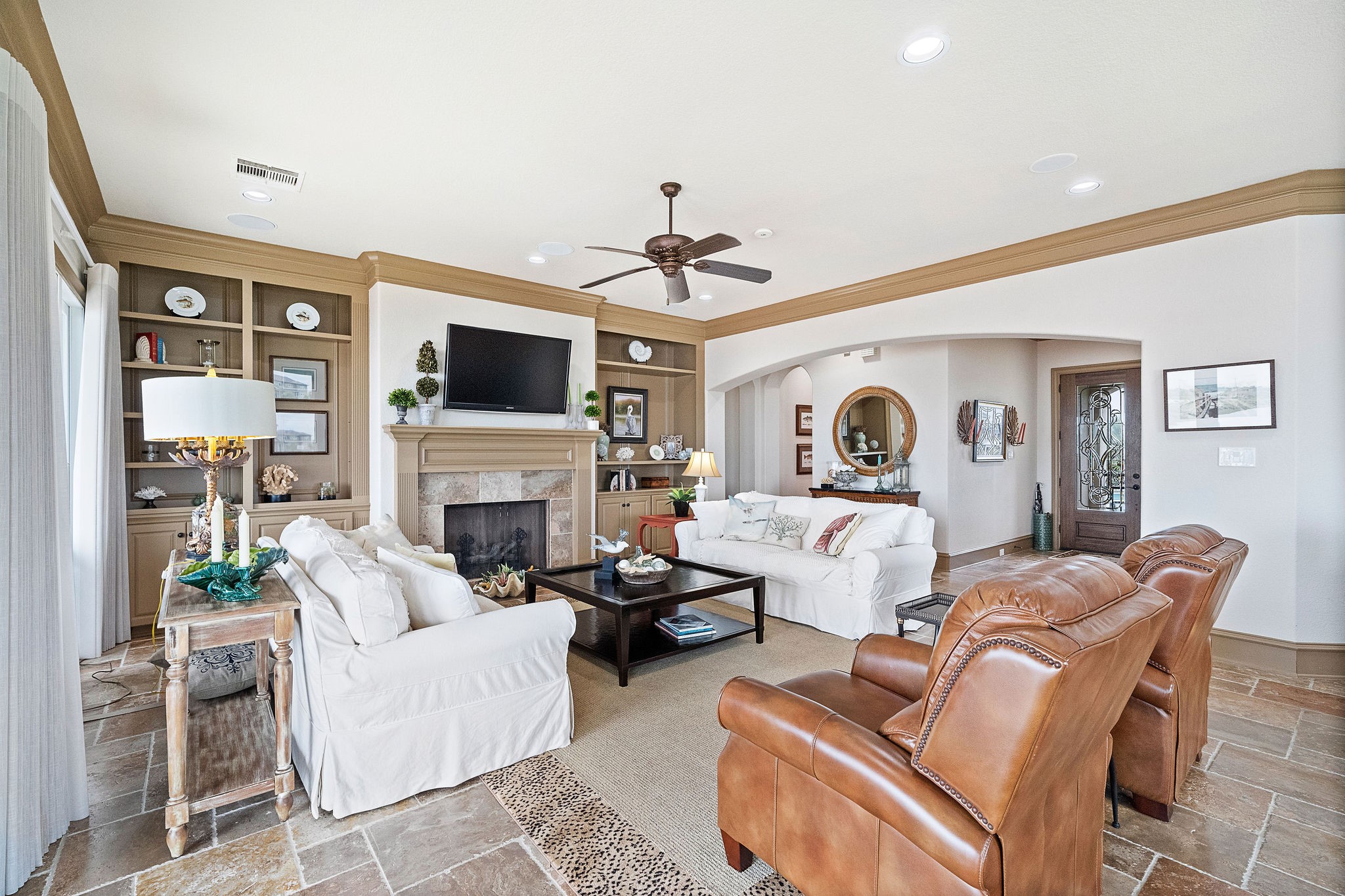 An open concept inviting living area, featuring a cozy fireplace, built-in cabinetry, and water views from every window throughout the home