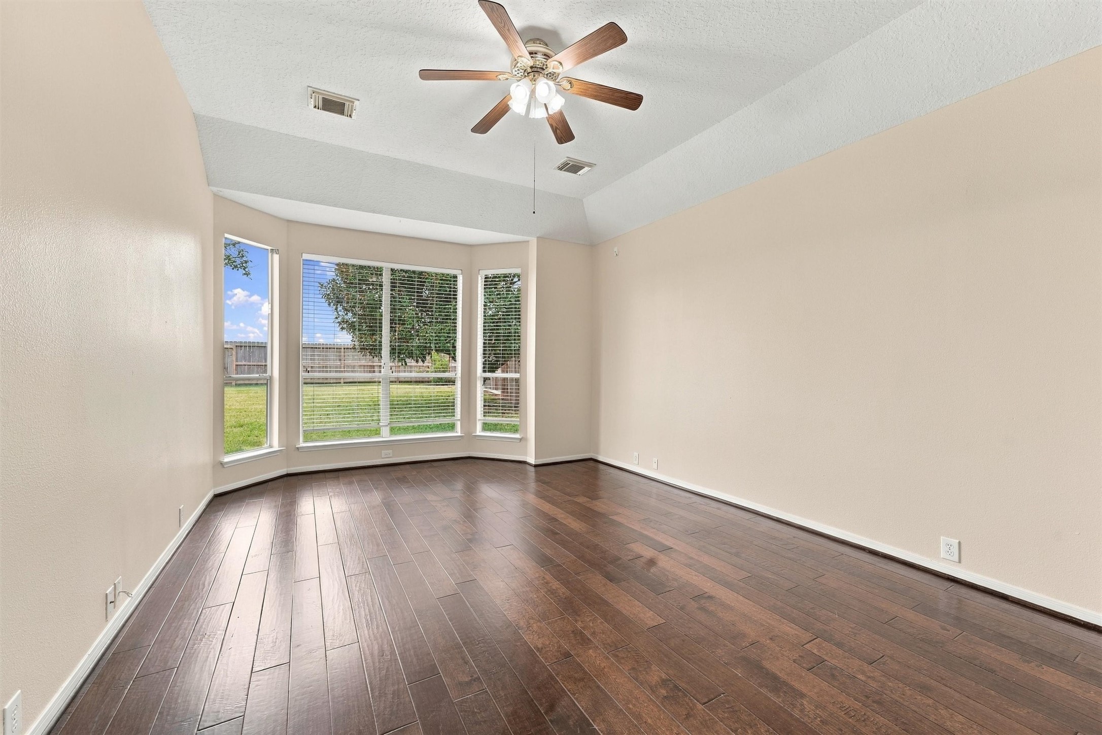 Spacious first floor primary bedroom featuring hardwood flooring, a ceiling fan, and backyard views.