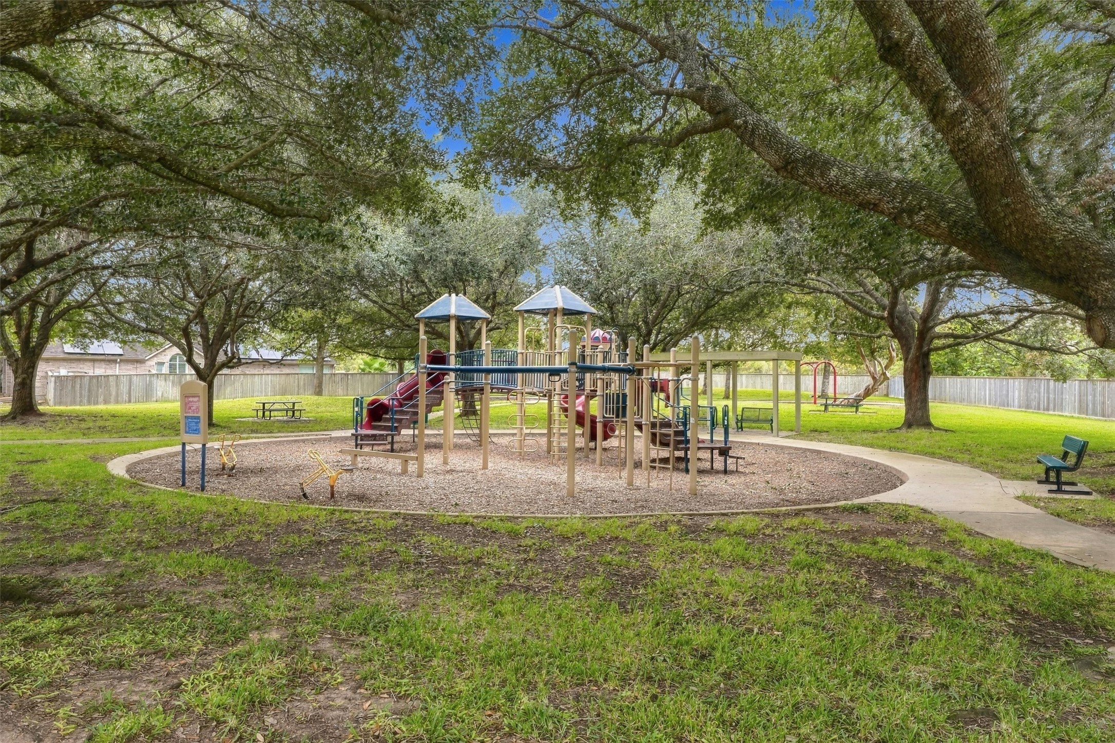 Neighborhood playground surrounded by mature shade trees and open green space.