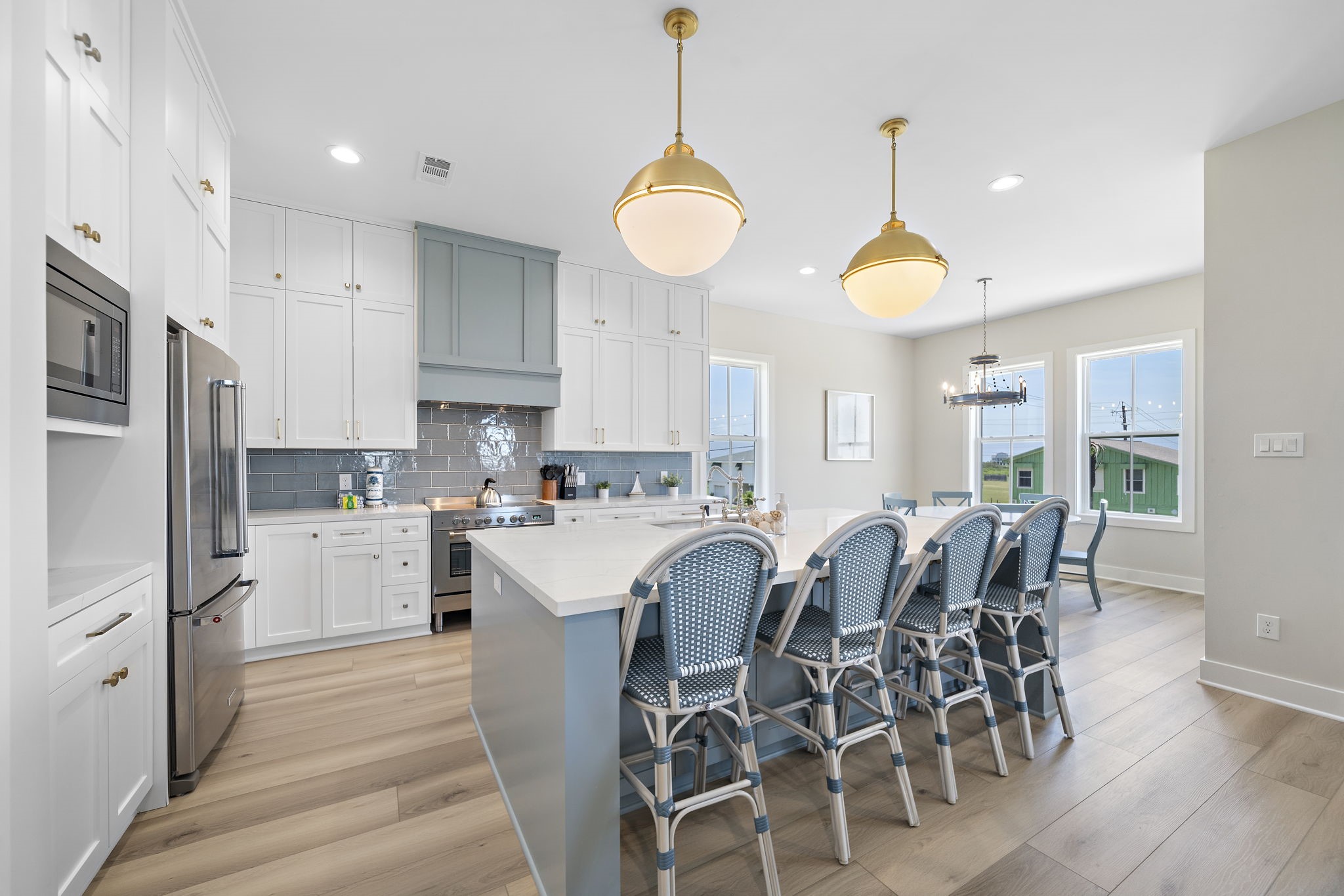 Bright and spacious kitchen featuring a large island with seating for six, elegant pendant lighting, and modern stainless steel appliances, complemented by crisp white cabinetry and a stylish blue tile backsplash. Bright and spacious kitchen featuring a large island with seating for six, elegant pendant lighting, and modern stainless steel appliances, complemented by crisp white cabinetry and a stylish blue tile backsplash.