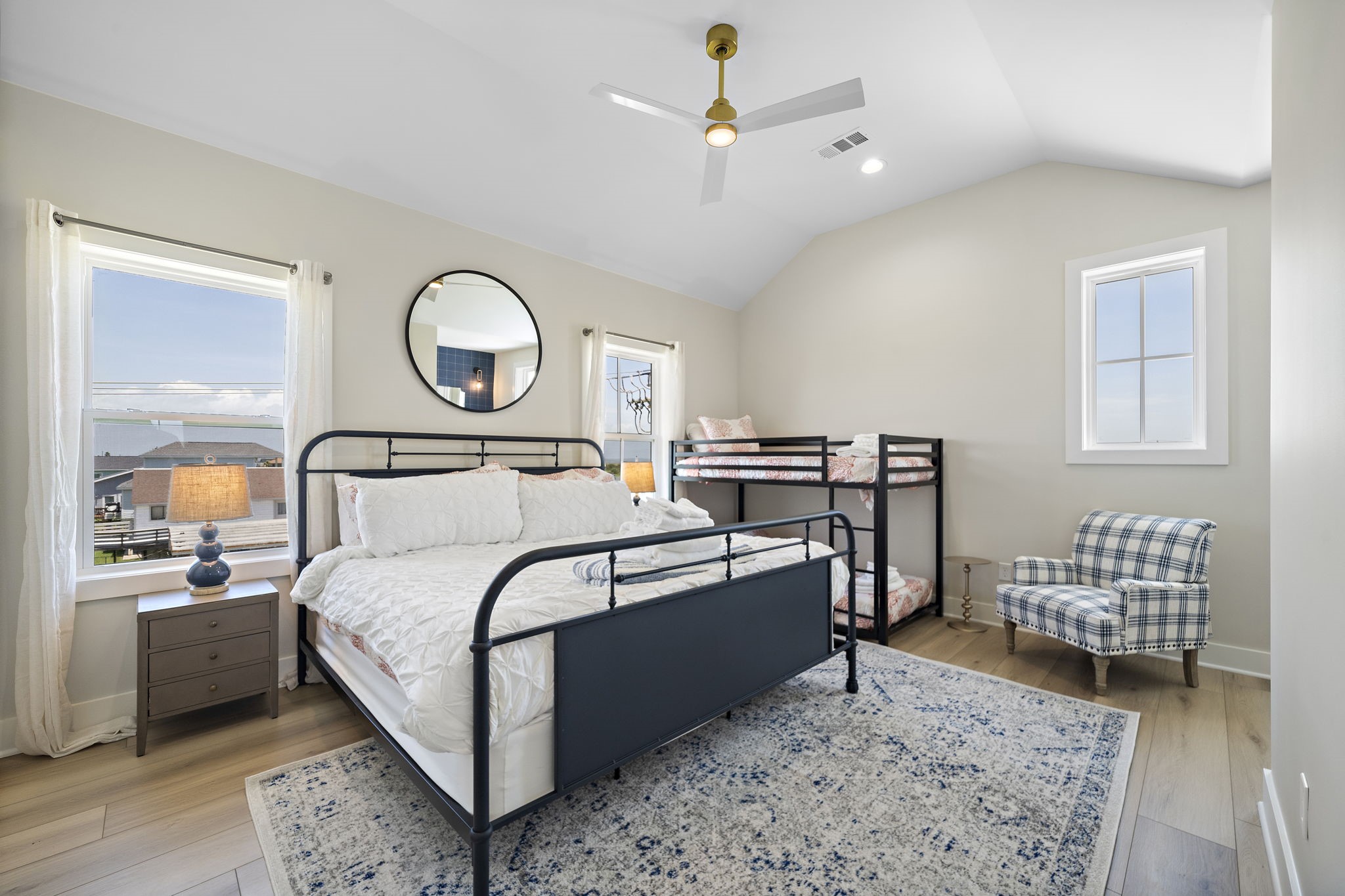 Bright and inviting bedroom featuring a stylish metal bed, cozy bunk beds, and a chic plaid armchair, all enhanced by natural light from large windows.