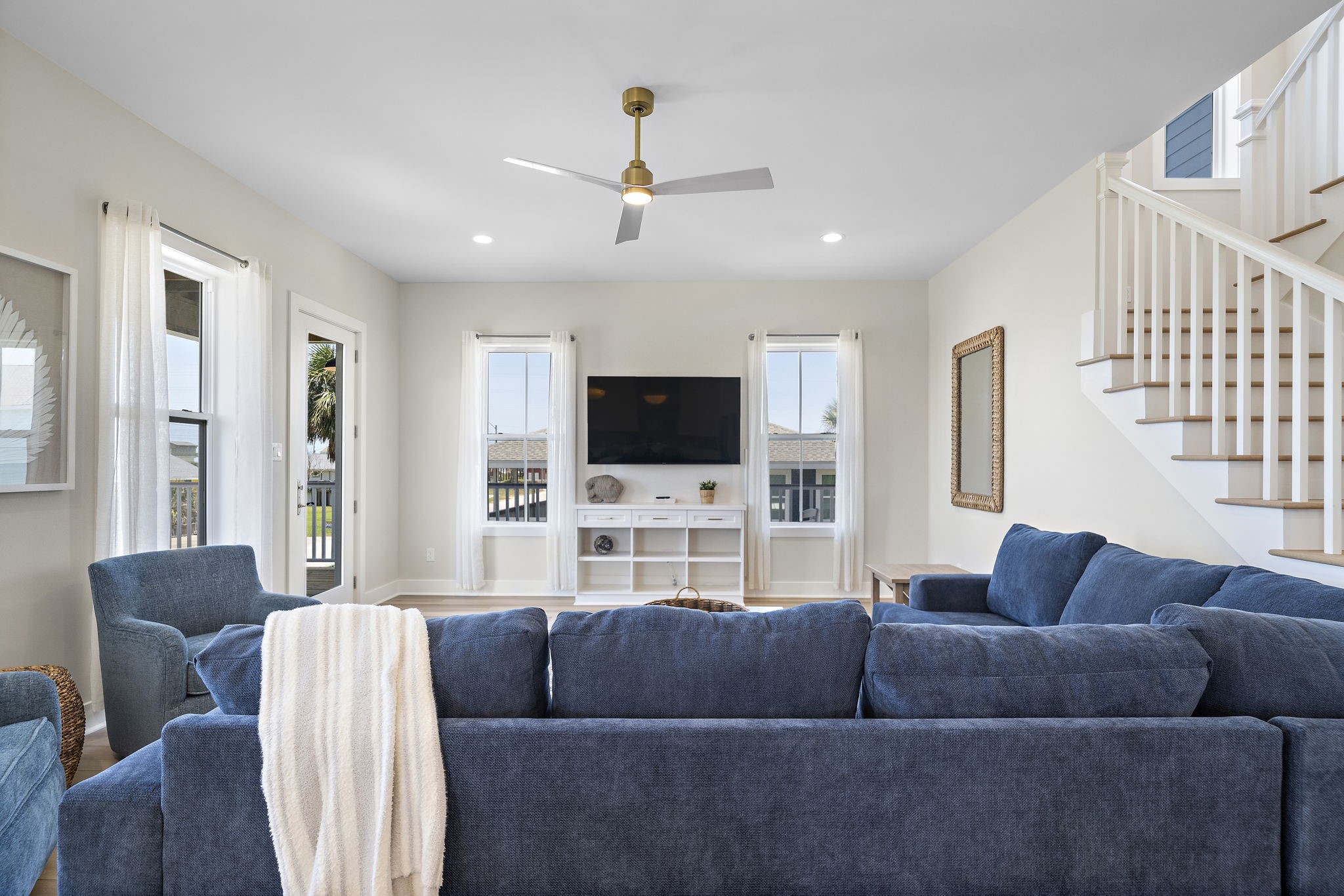Spacious living room with abundant natural light, featuring a cozy blue sectional, ceiling fan, and modern entertainment center. Spacious living room with abundant natural light, featuring a cozy blue sectional, ceiling fan, and modern entertainment center.