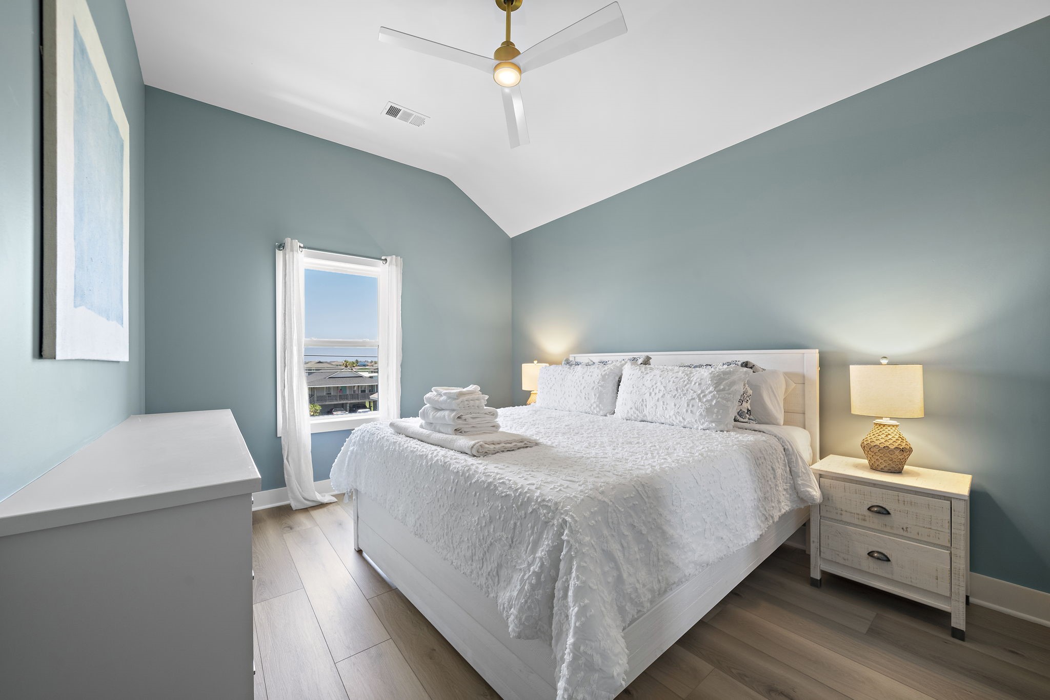 Serene bedroom with soothing blue walls, a comfortable bed, and ample natural light from a well-placed window, creating a cozy and inviting atmosphere.