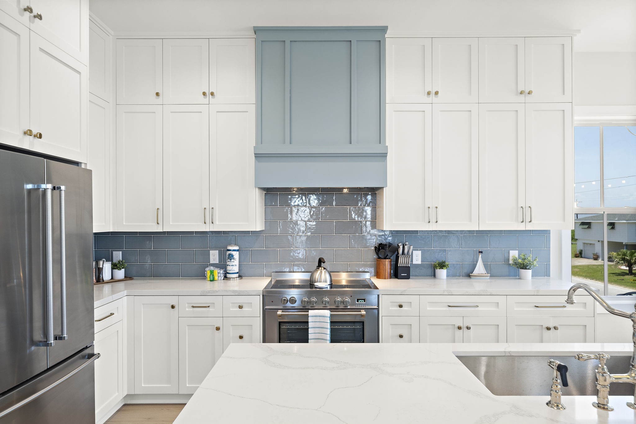 Bright and inviting kitchen with sleek stainless steel appliances, elegant white cabinetry, and a stylish blue tile backsplash.