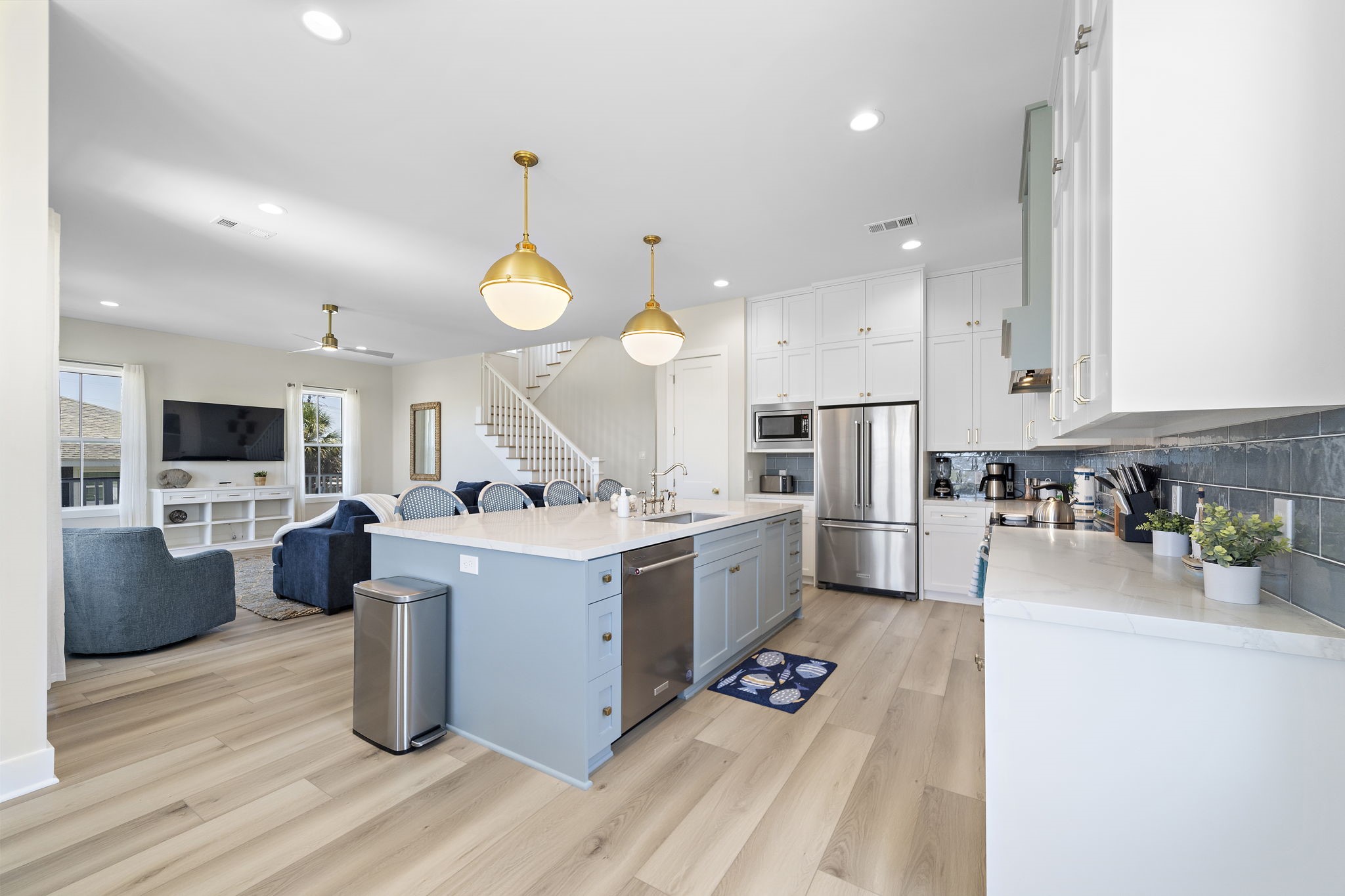 Spacious open-concept kitchen and living area featuring a large island with elegant pendant lighting, stainless steel appliances, and ample cabinetry, seamlessly flowing into a cozy living room with a modern staircase. Spacious open-concept kitchen and living area featuring a large island with elegant pendant lighting, stainless steel appliances, and ample cabinetry, seamlessly flowing into a cozy living room with a modern staircase.