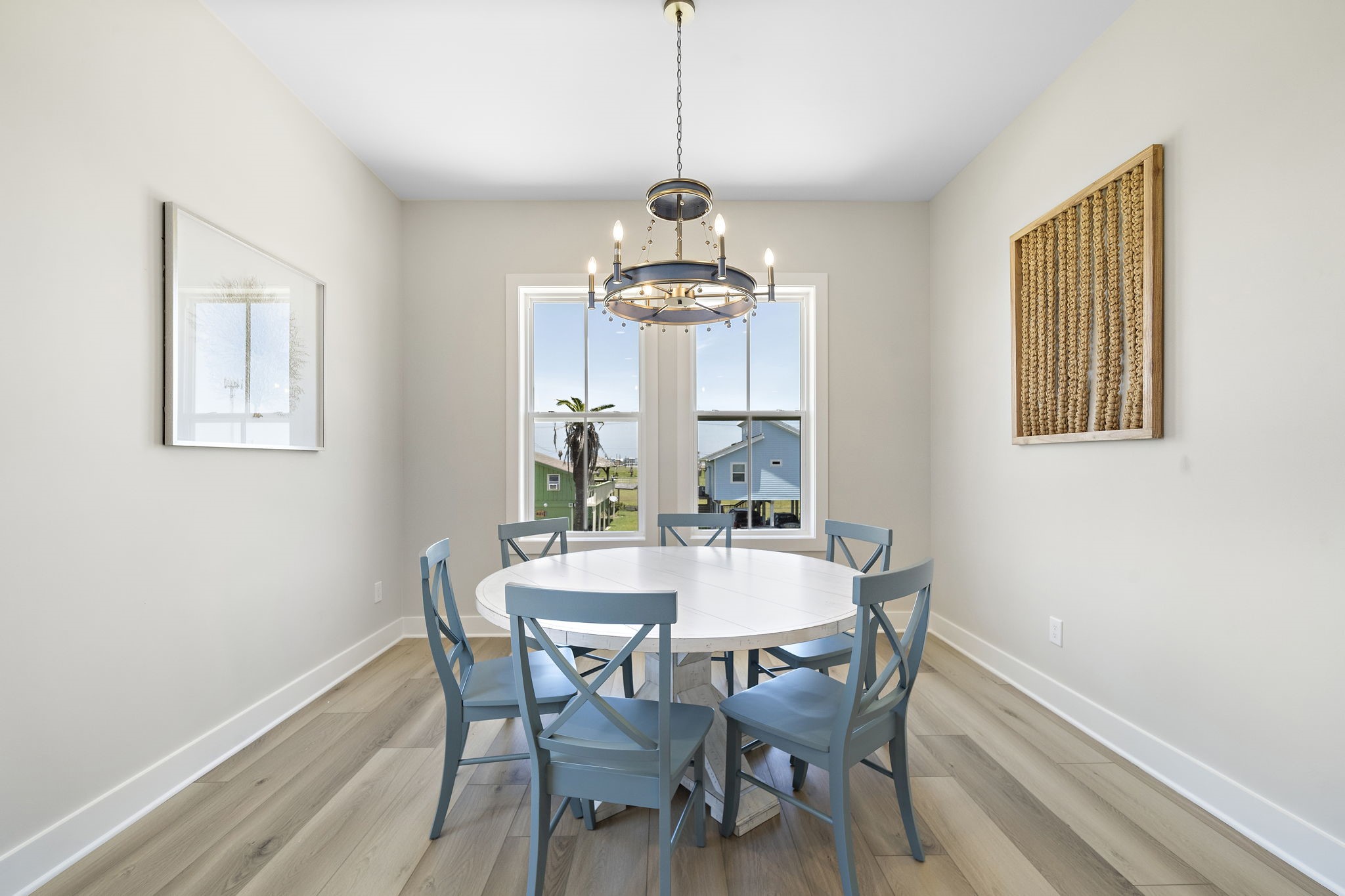 Bright dining area featuring a round table with blue chairs, complemented by a modern chandelier and large window offering scenic views.