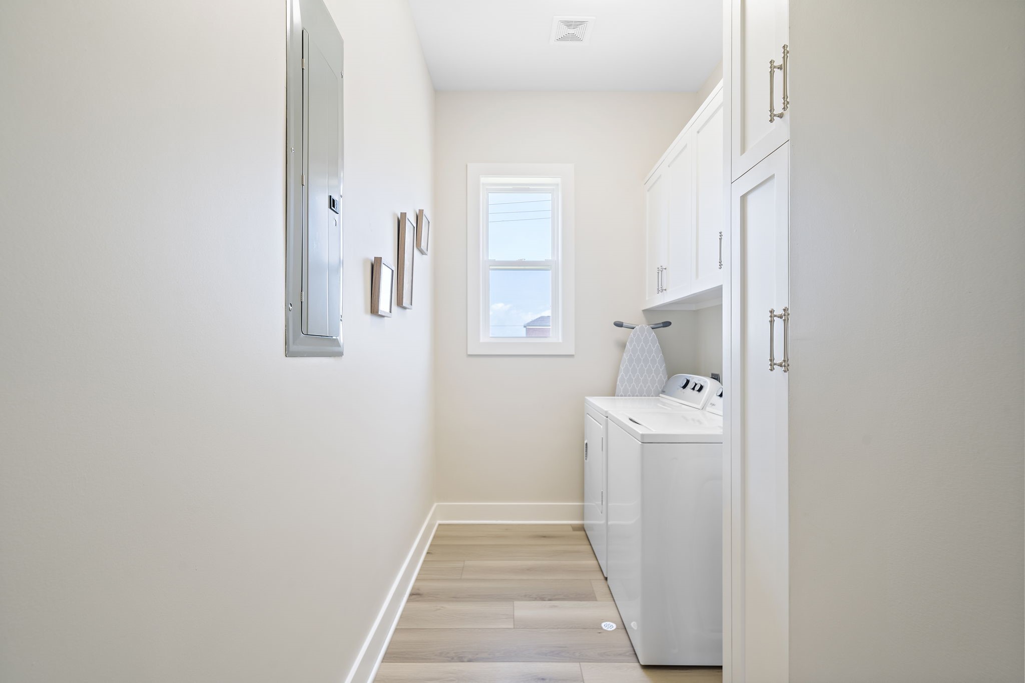 Bright and efficient laundry room featuring sleek white cabinetry, modern washer and dryer, and natural light from the window.
