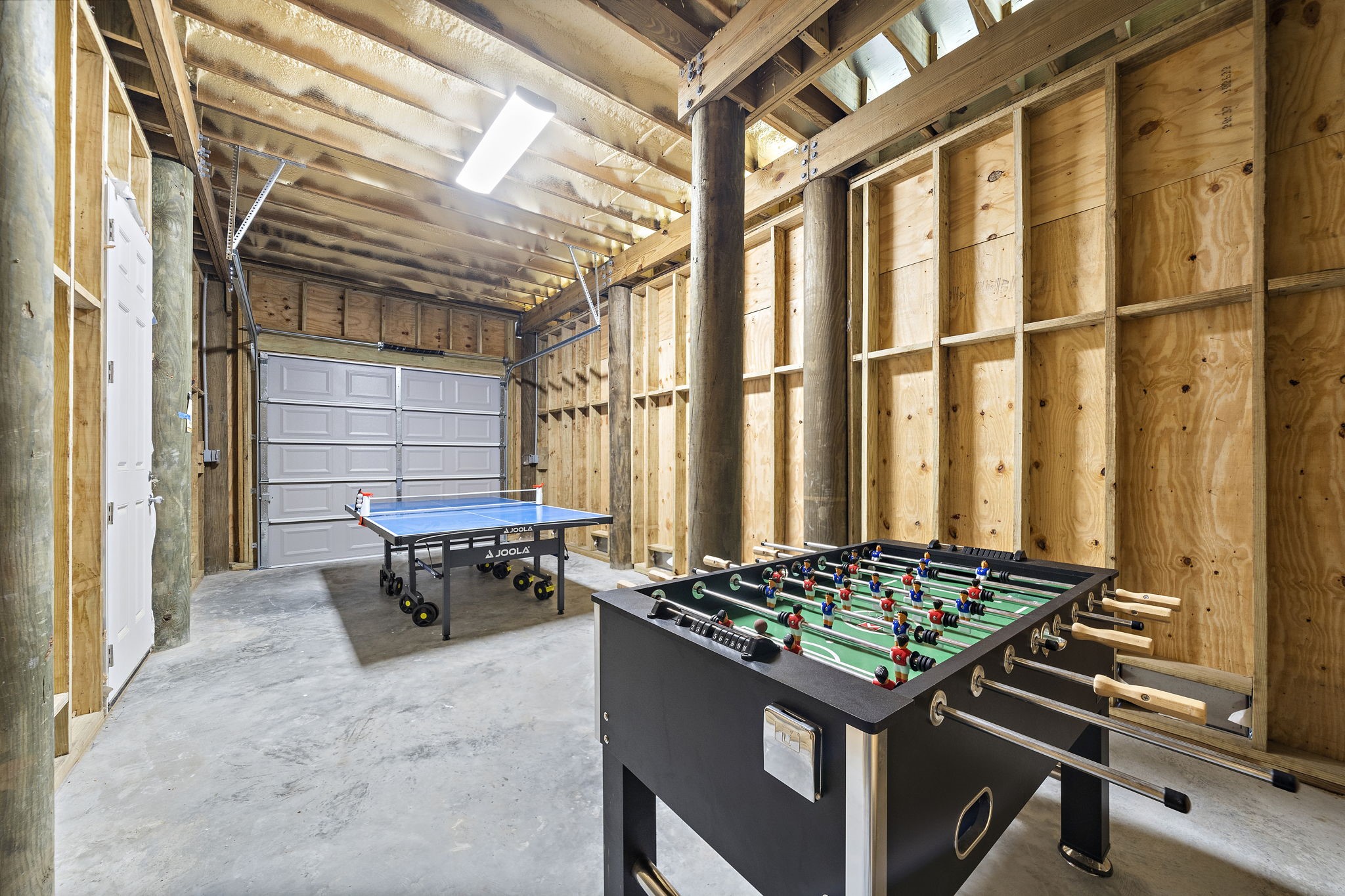 Spacious game room with a foosball table and ping pong setup, featuring rustic wood walls and ample lighting for entertainment.