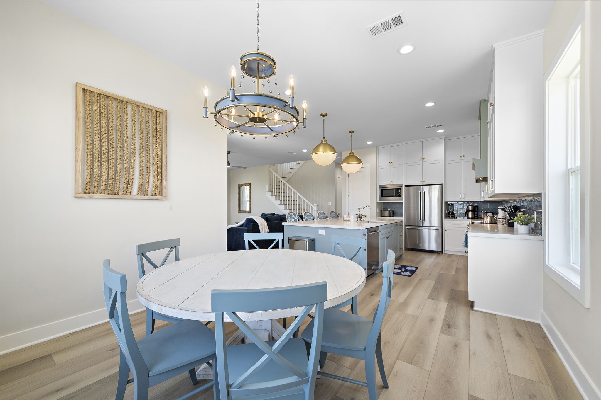 Bright and open dining area with a charming chandelier, adjacent to a modern kitchen featuring an island, stainless steel appliances, and ample cabinetry.