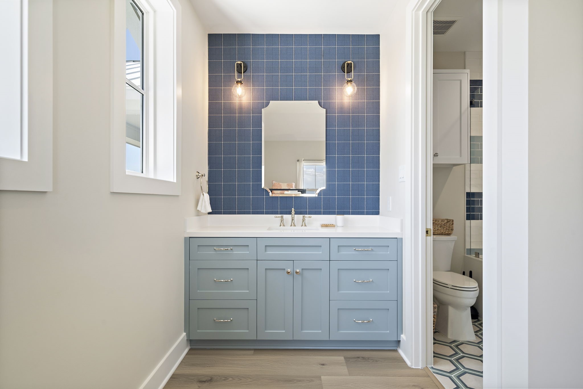 Charming bathroom featuring a stylish blue vanity with ample storage, complemented by a chic blue tile backsplash and modern lighting.