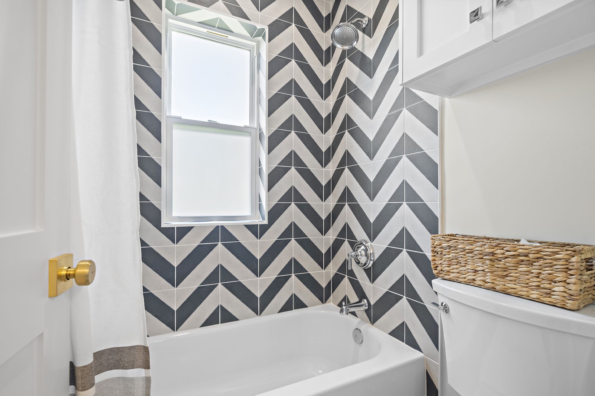 Stylish bathroom featuring a chic chevron tile design, a modern showerhead, and a bright window, offering a fresh and inviting feel.