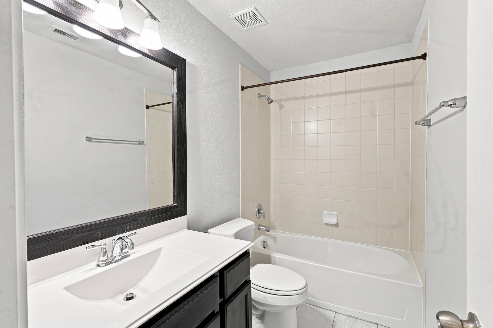 Secondary bathroom with tub/shower combination, large framed mirror, and dark cabinetry.