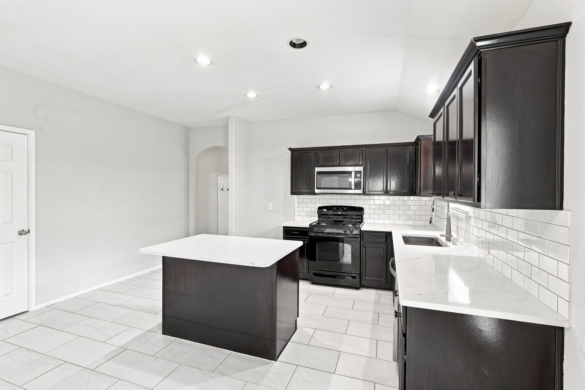 Kitchen featuring dark cabinetry, white countertops, subway tile backsplash, stainless steel appliances, and center island.