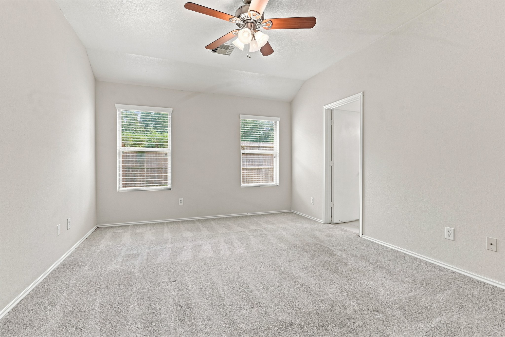 Spacious primary bedroom with vaulted ceiling, ceiling fan, neutral carpet, and multiple windows.