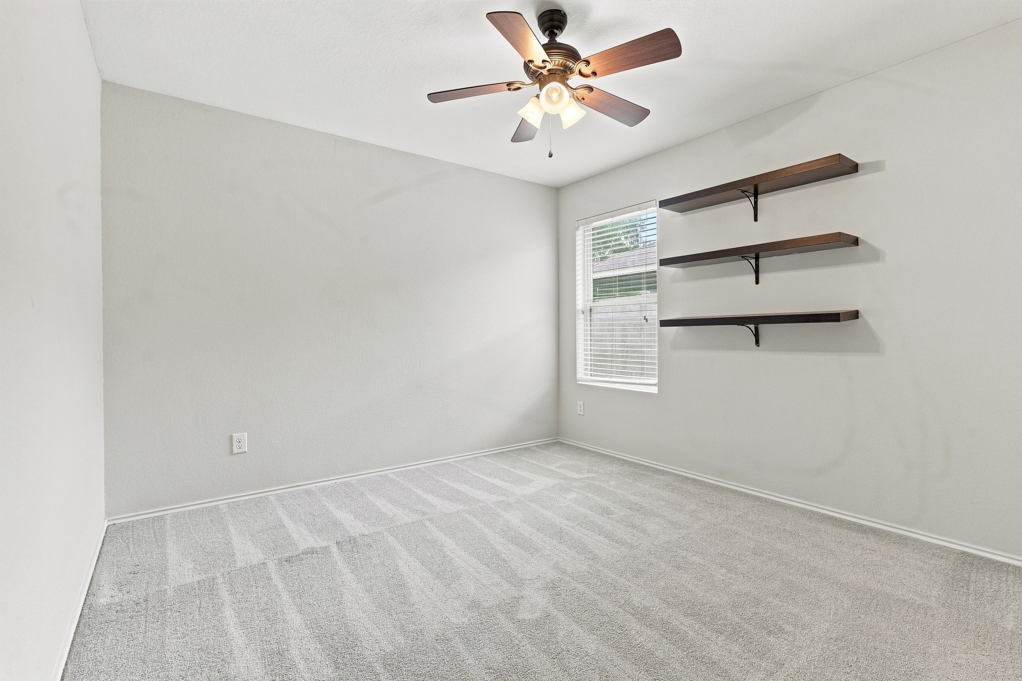 Second bedroom with ceiling fan, window, and floating wall shelves