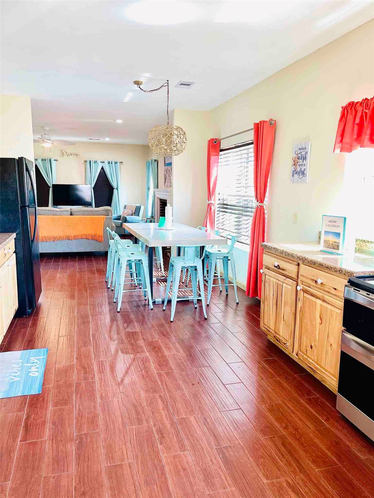 Bright and inviting open-concept living space with a spacious kitchen, featuring natural wood cabinets, a large dining area with turquoise chairs, and a cozy living room perfect for relaxation.