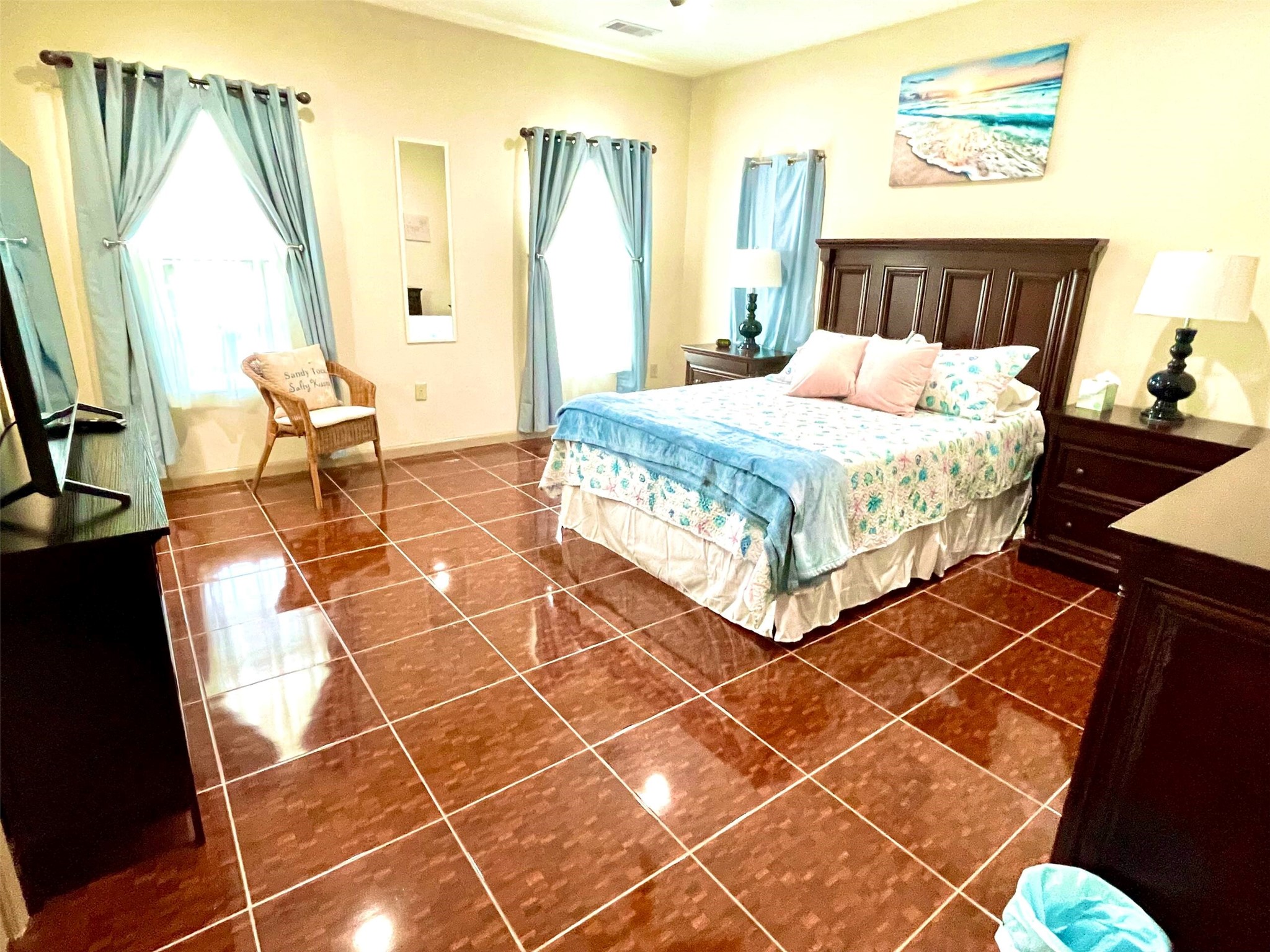 Spacious bedroom with glossy tile floors, elegant dark wood furniture, and soft blue accents, creating a serene and inviting atmosphere.