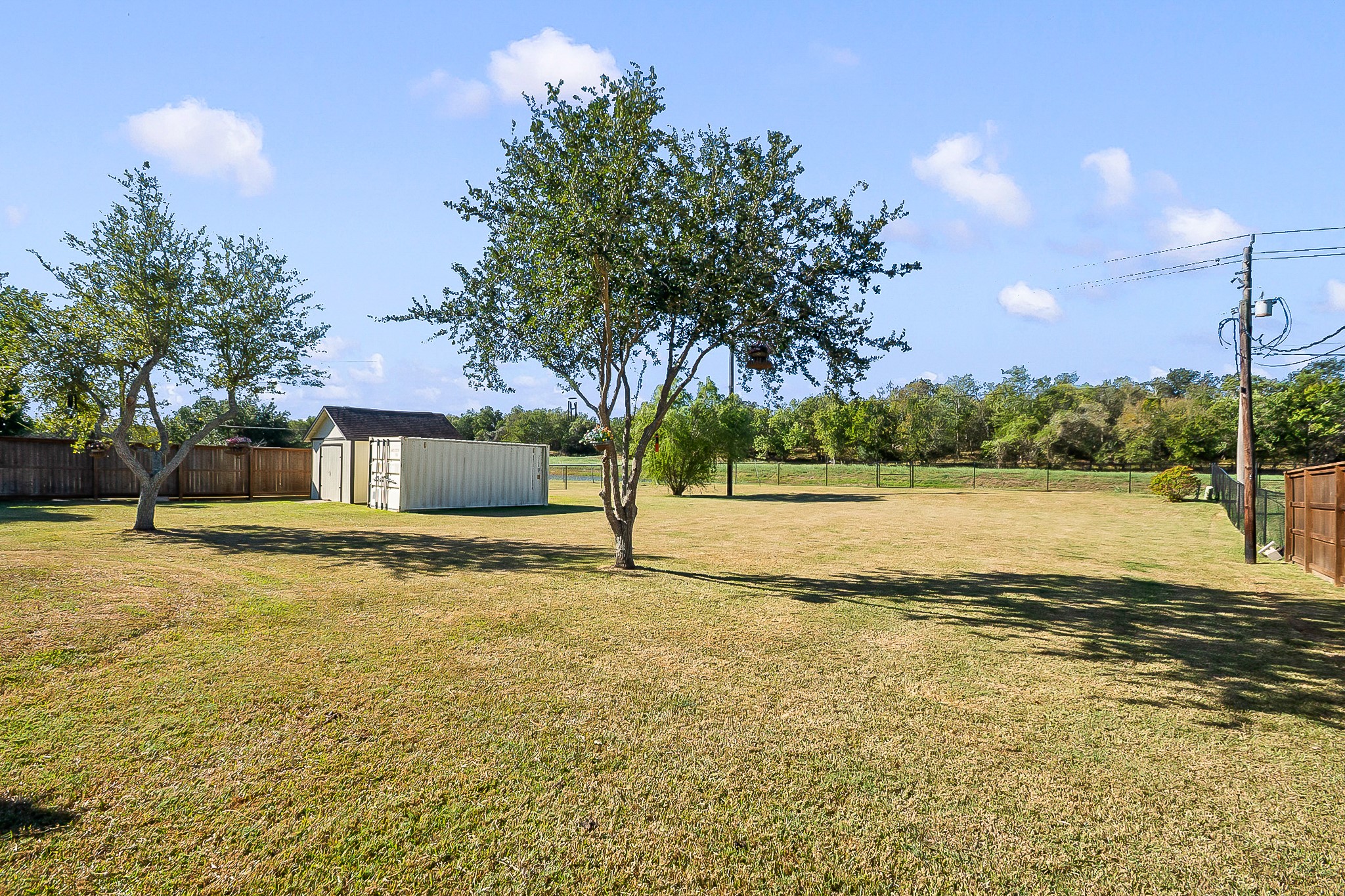 Expansive backyard with lush green lawn, mature trees, and ample space for outdoor activities, complemented by a privacy fence that backs up to the view of the water.